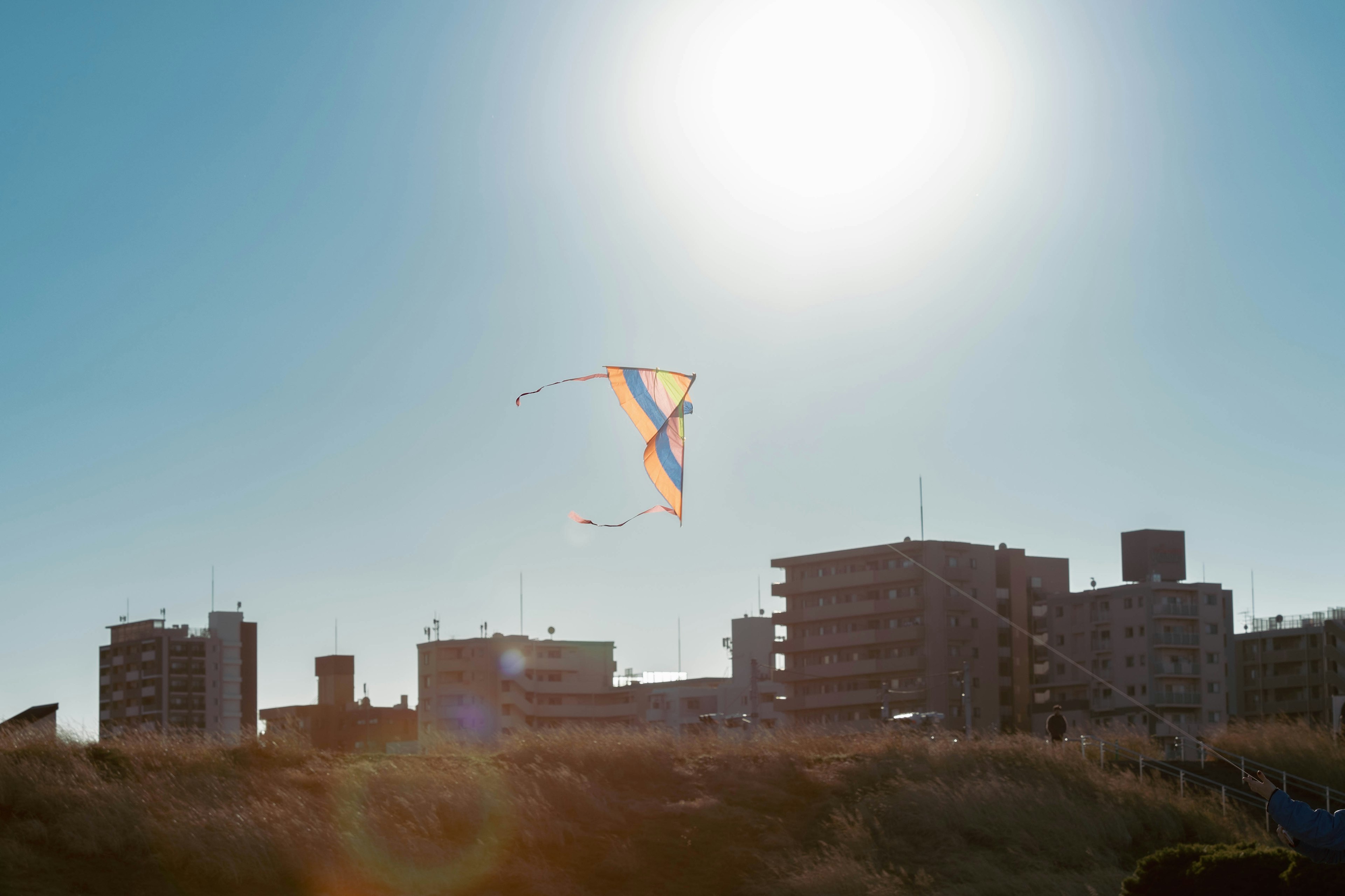 A colorful kite flying against a clear blue sky with city buildings in silhouette