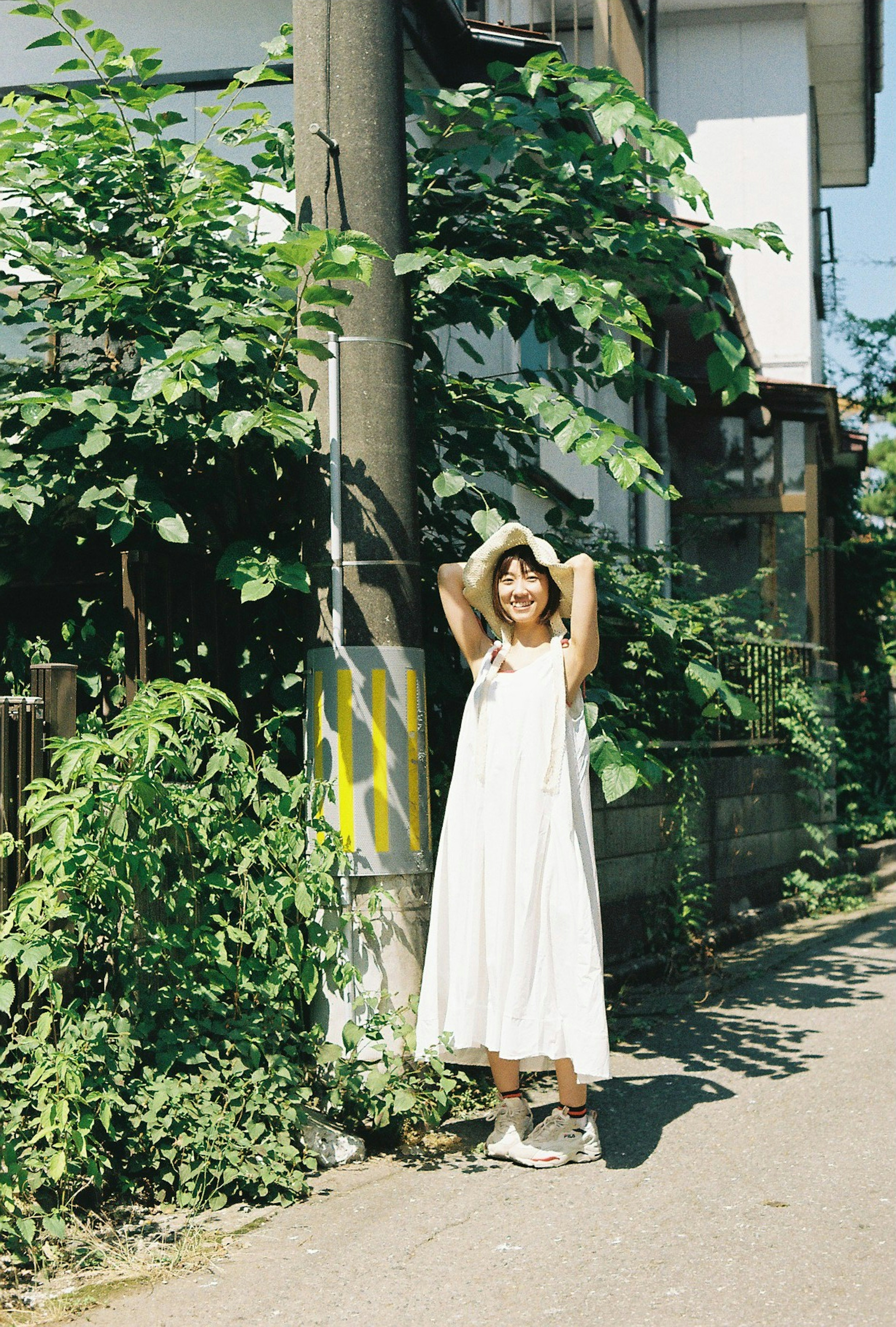 Une femme en robe blanche se tient au milieu d'une verdure luxuriante à un coin de rue