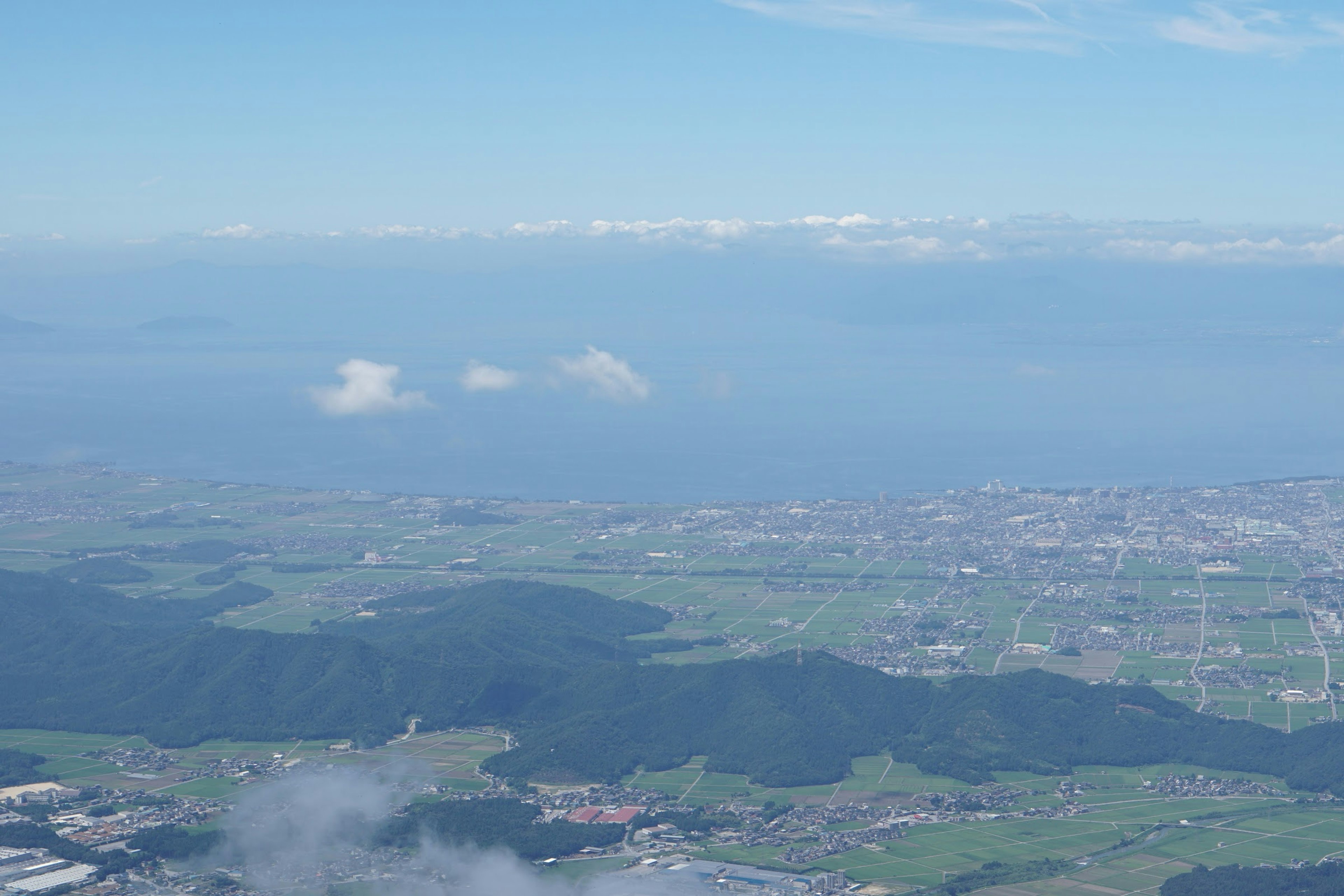 青い海と雲が広がる風景に、緑豊かな土地と都市が見える