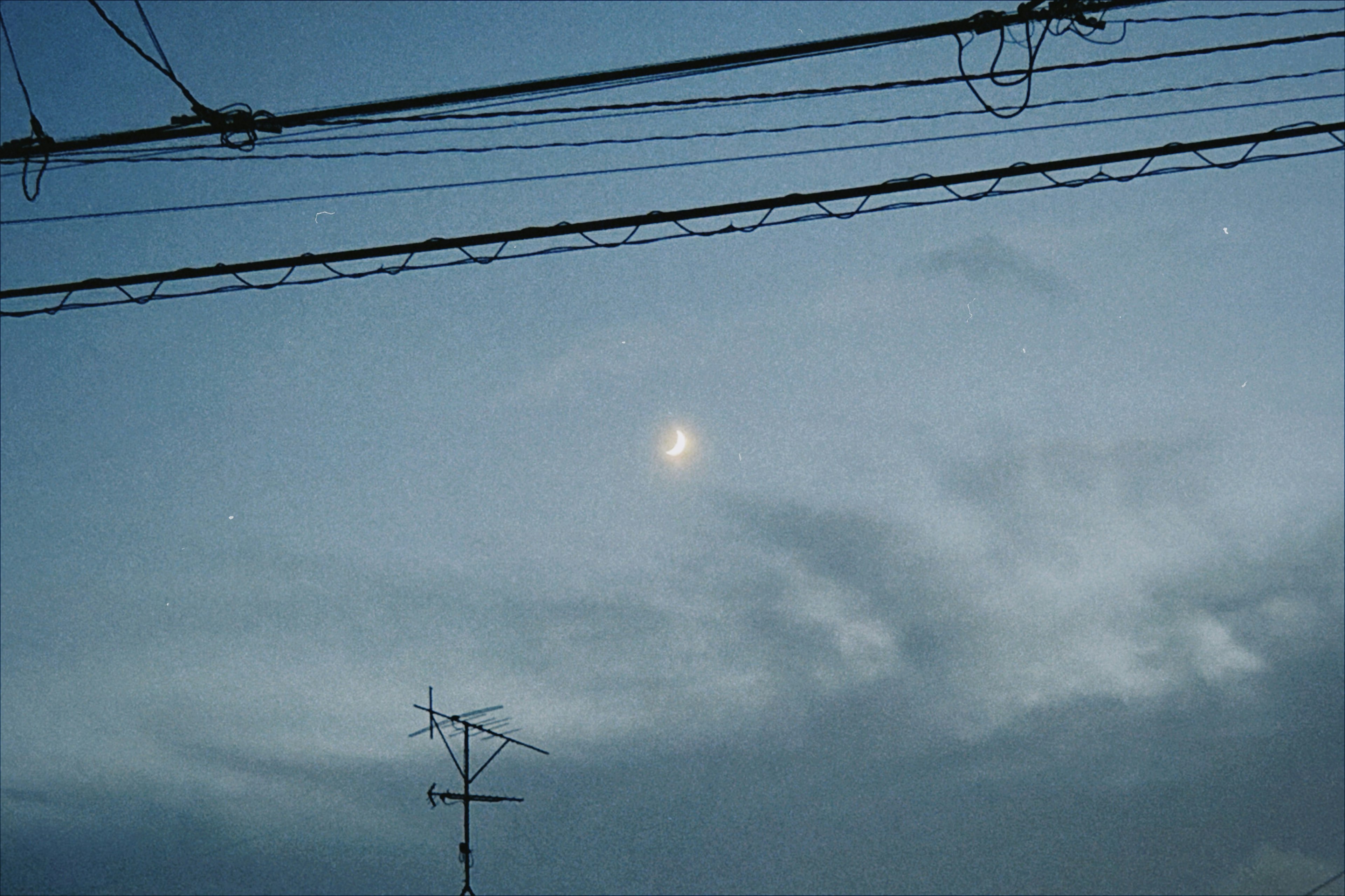 A view of the moon in a cloudy sky with power lines crossing the image