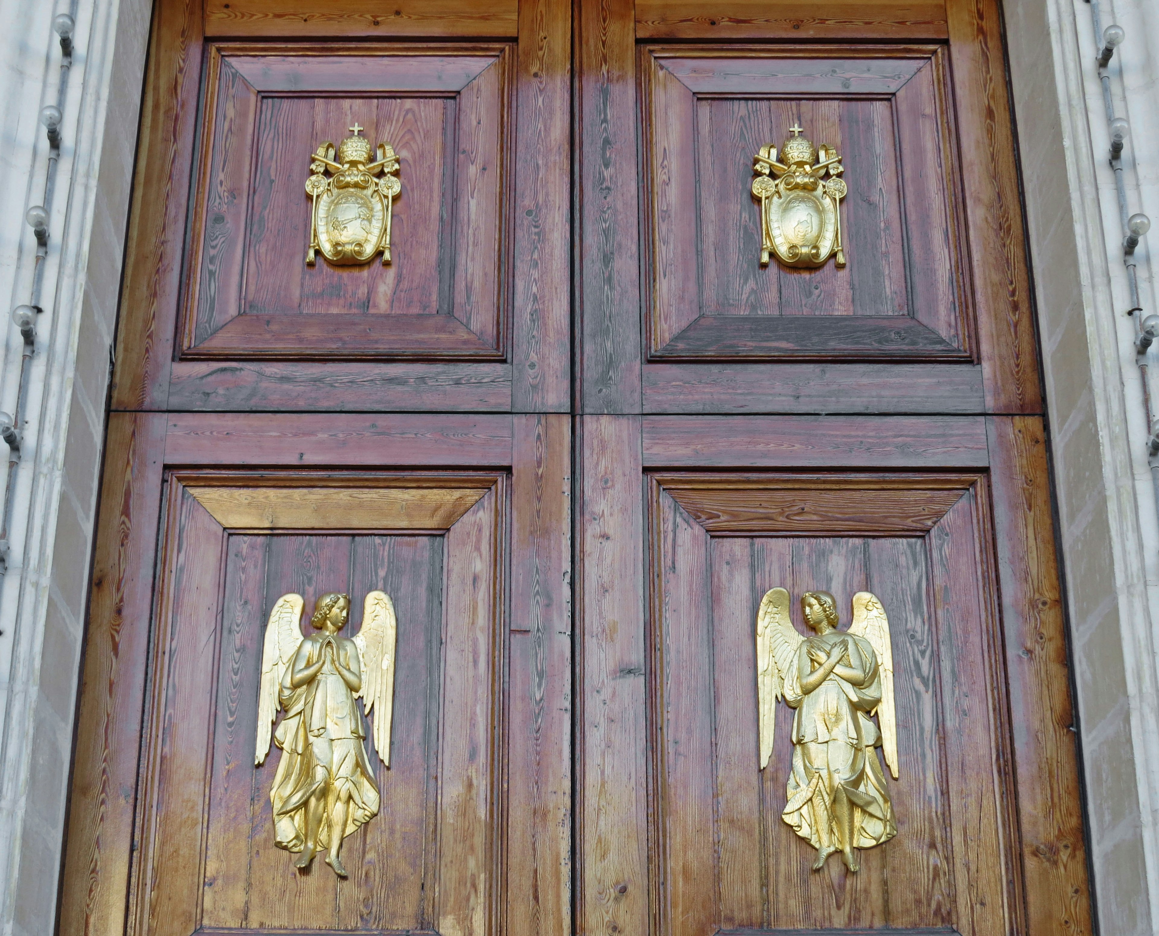 Puerta de madera con esculturas de ángeles dorados y escudos