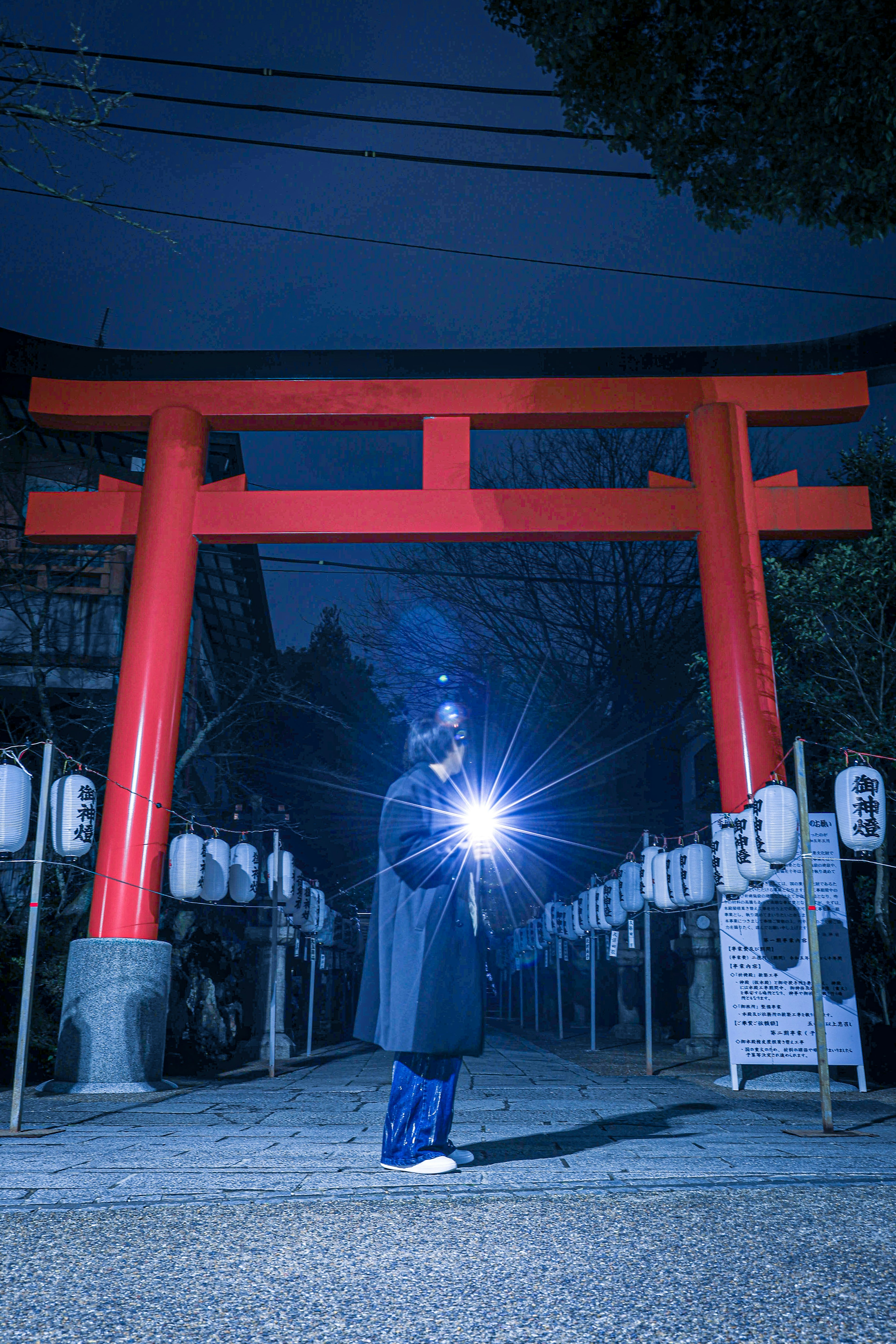 Una persona in piedi davanti a un torii rosso di notte con una torcia