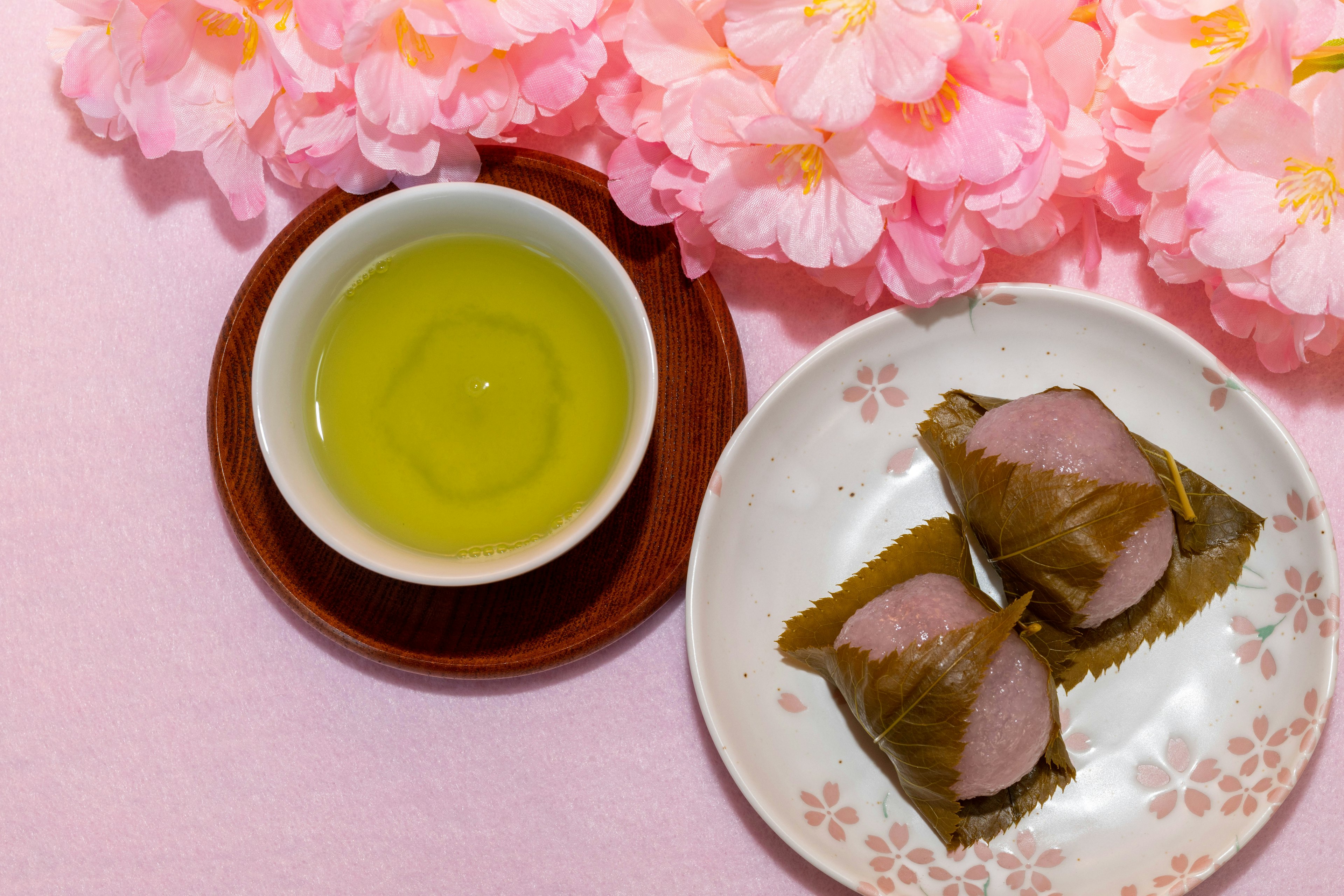 A plate with traditional Japanese sweets and green tea against a pink cherry blossom background