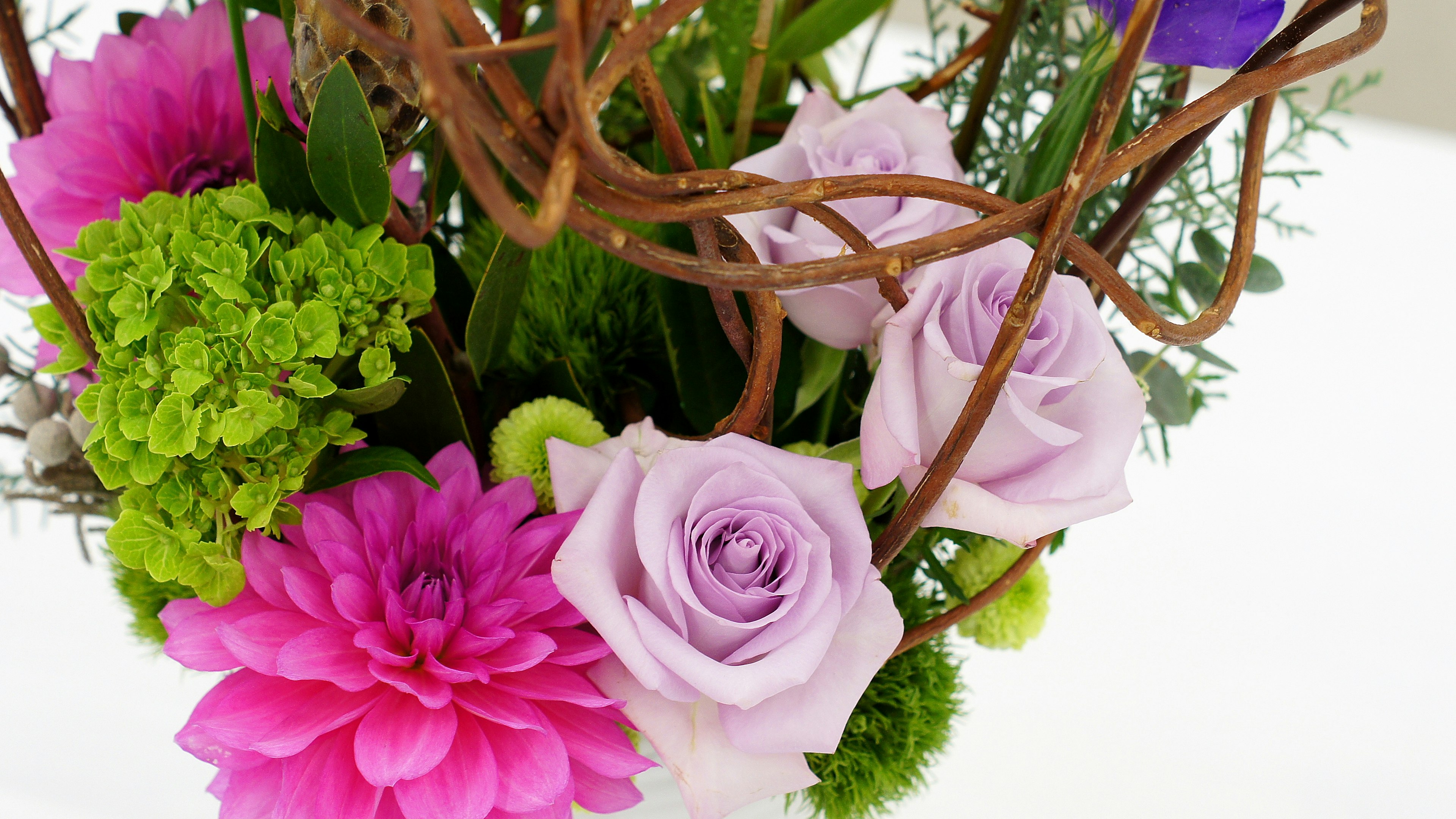 Un bouquet vivace con rose viola pallido e dalie rosa, fiori verdi e rami intrecciati