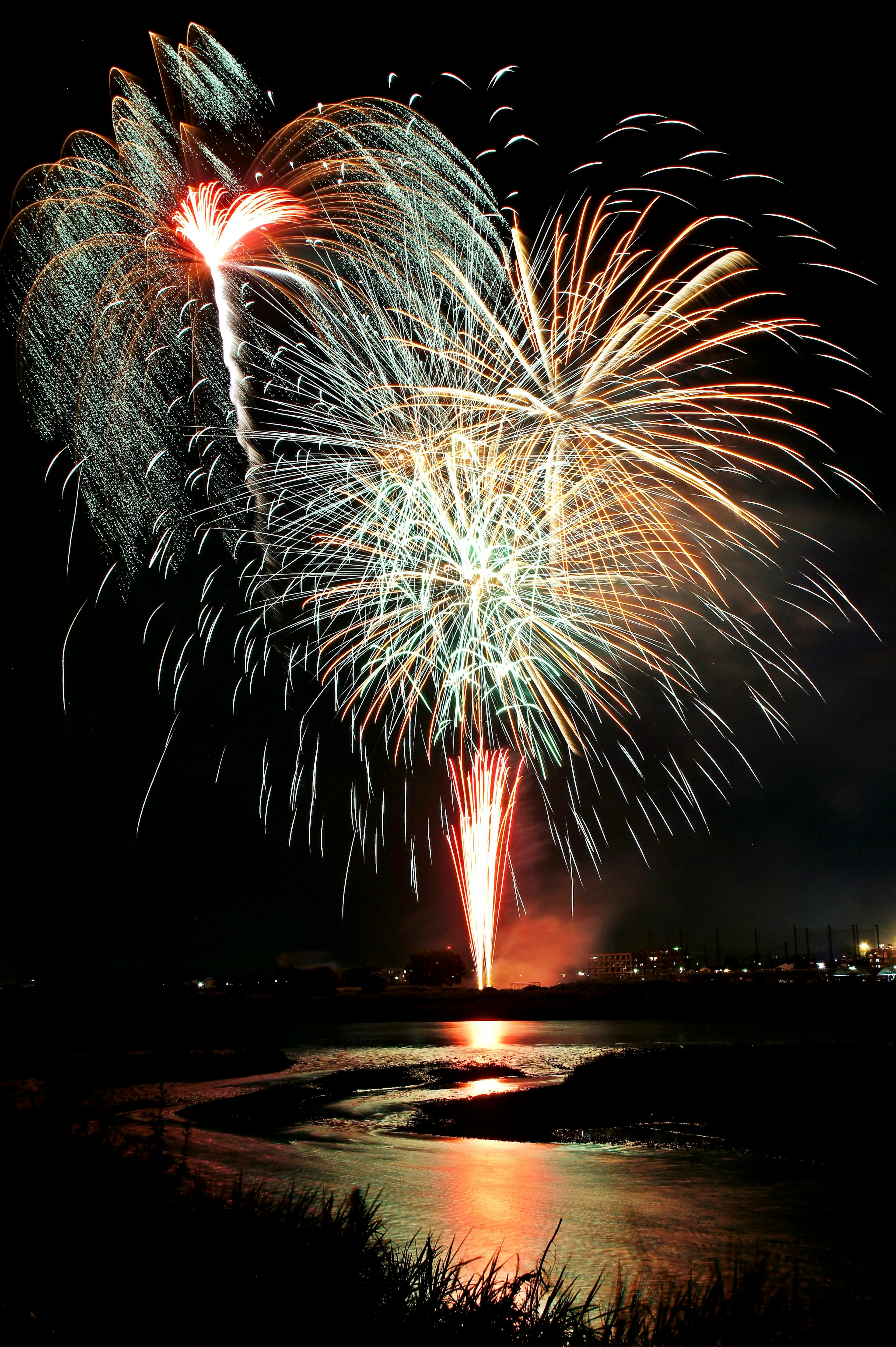 Fuegos artificiales coloridos estallando en el cielo nocturno sobre un río