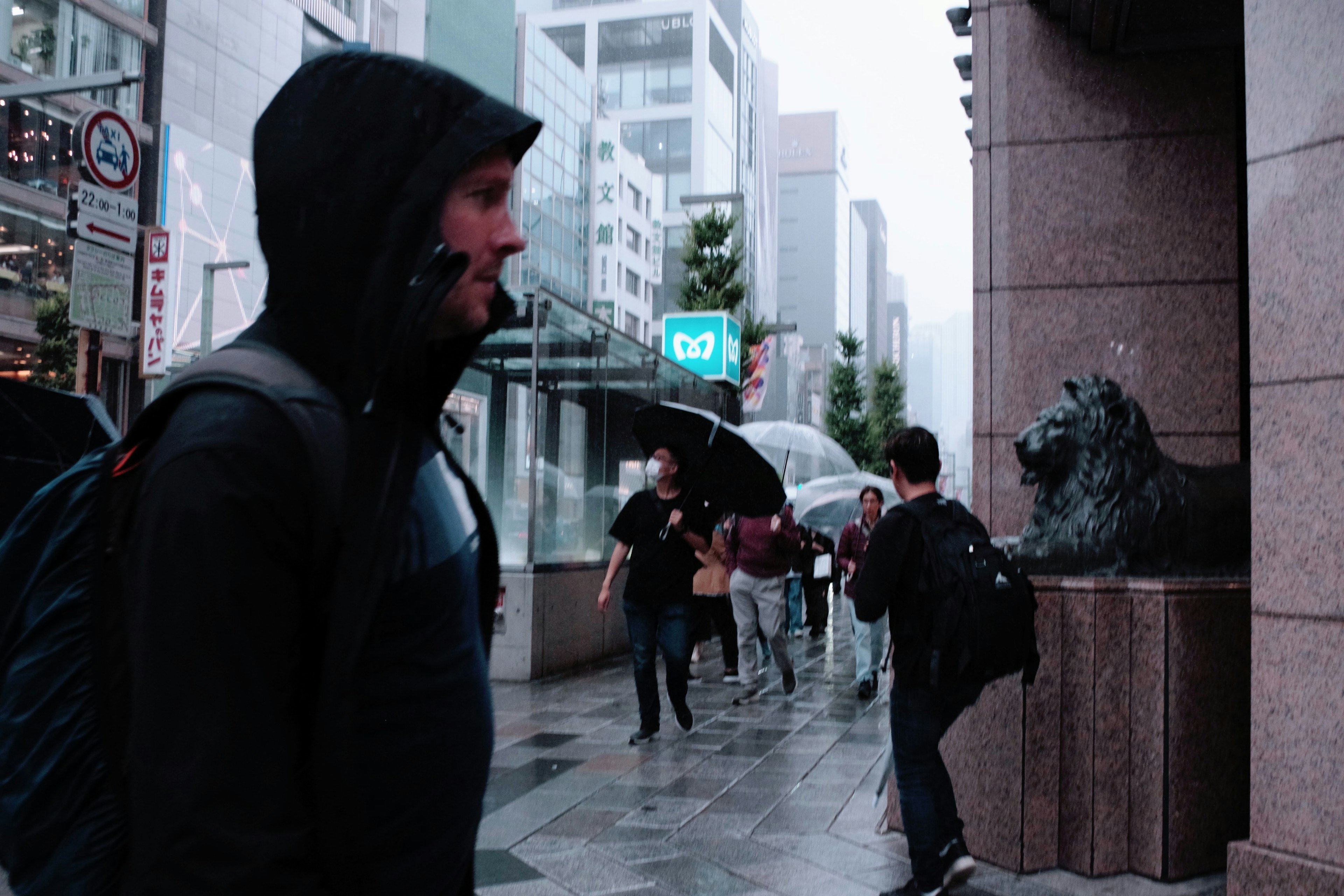 A man in a black hooded jacket walking in a rainy urban setting