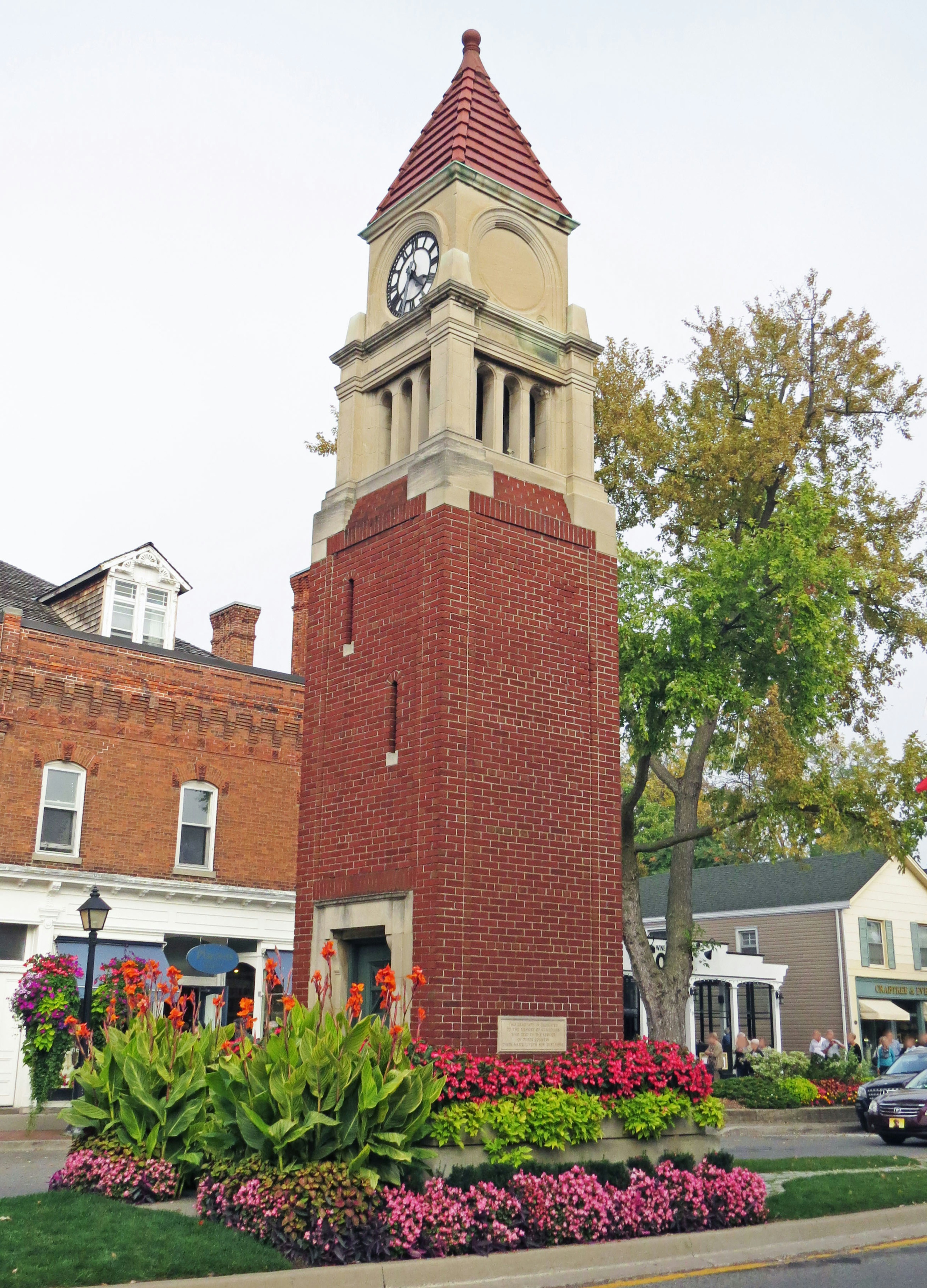 Brick clock tower surrounded by vibrant flowers and greenery