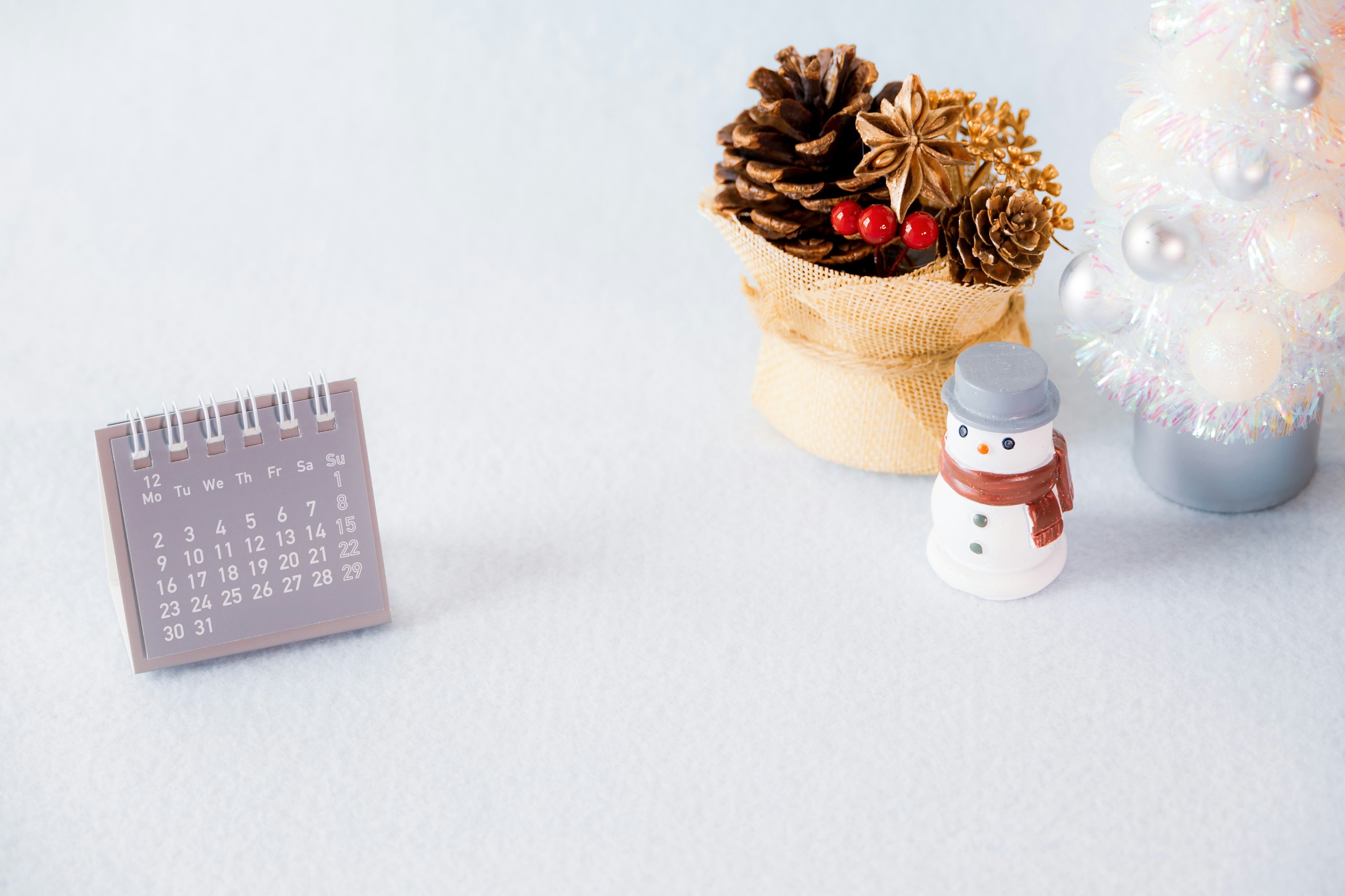 Small calendar with pine cone decoration and a snowman figurine in a winter setting