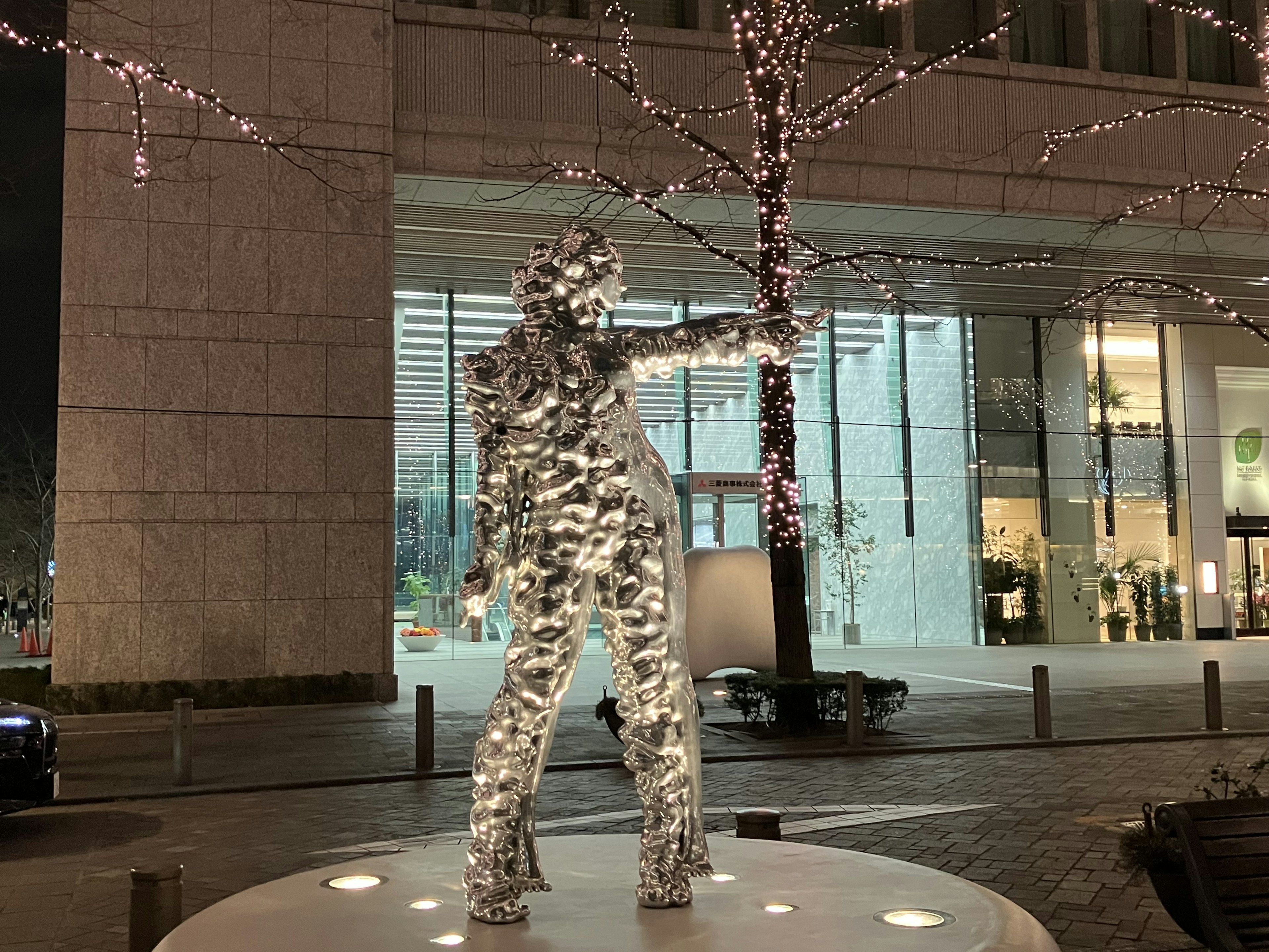 Escultura iluminada de una figura humana de pie en una ciudad de noche