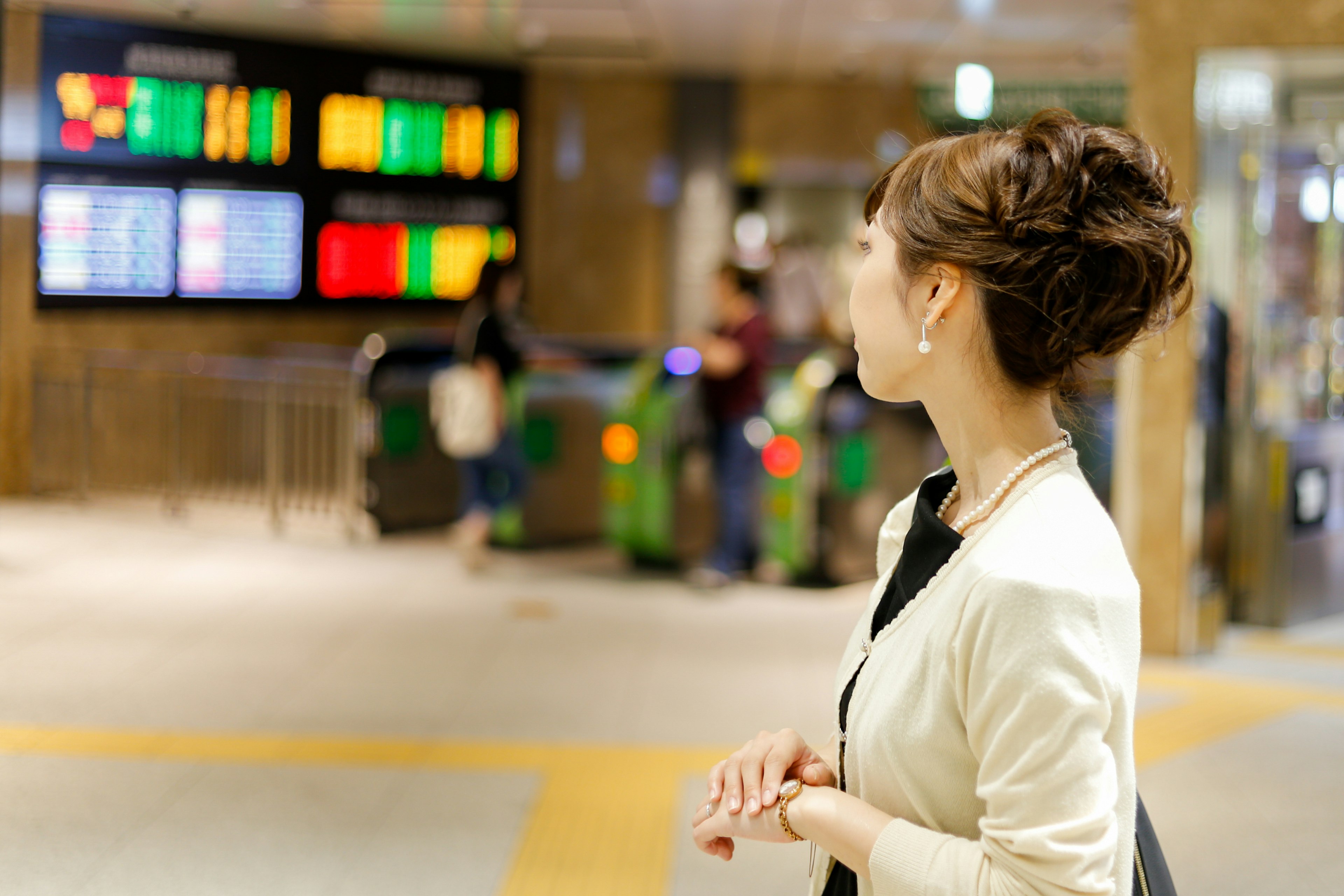 Una mujer esperando en la puerta de una estación con señales de destino y un fondo concurrido