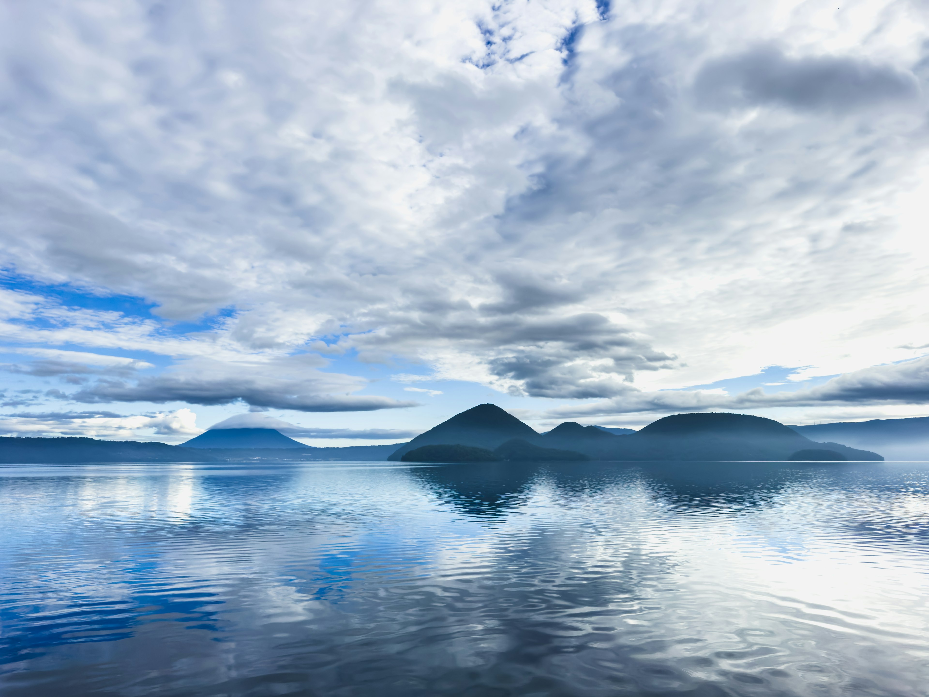 Pemandangan tenang danau dengan gunung yang memantul di air tenang dan langit biru