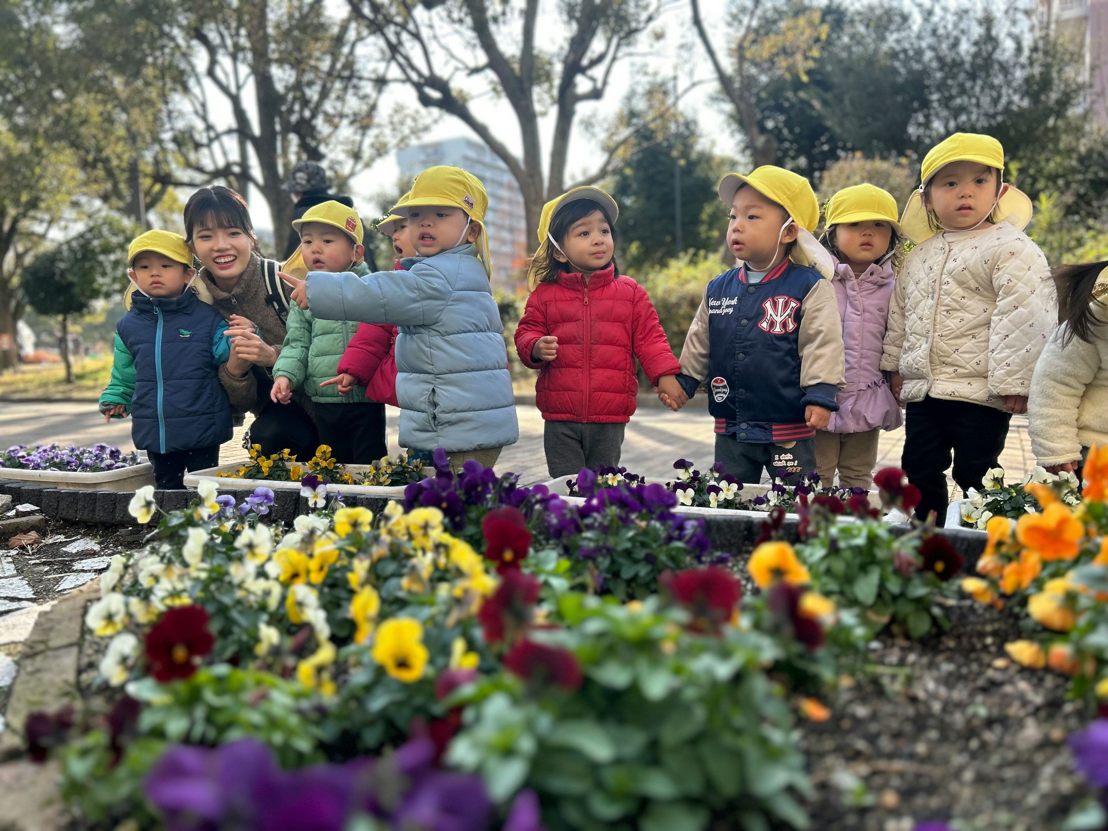 黄色い帽子をかぶった子供たちが花の前で笑顔でポーズをとっている