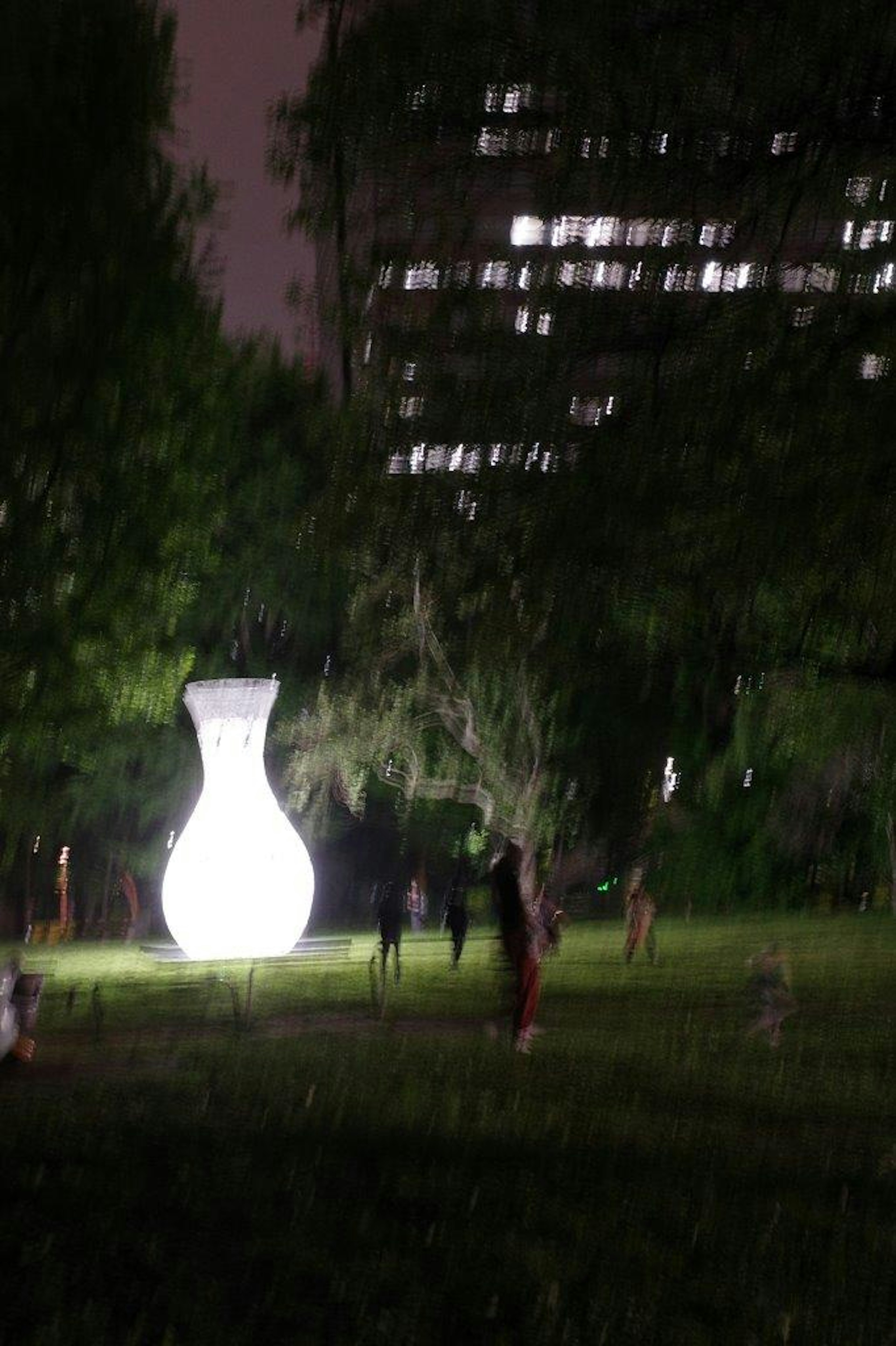 Große weiße Vasen-Skulptur in einem nächtlichen Park mit Menschen in der Nähe