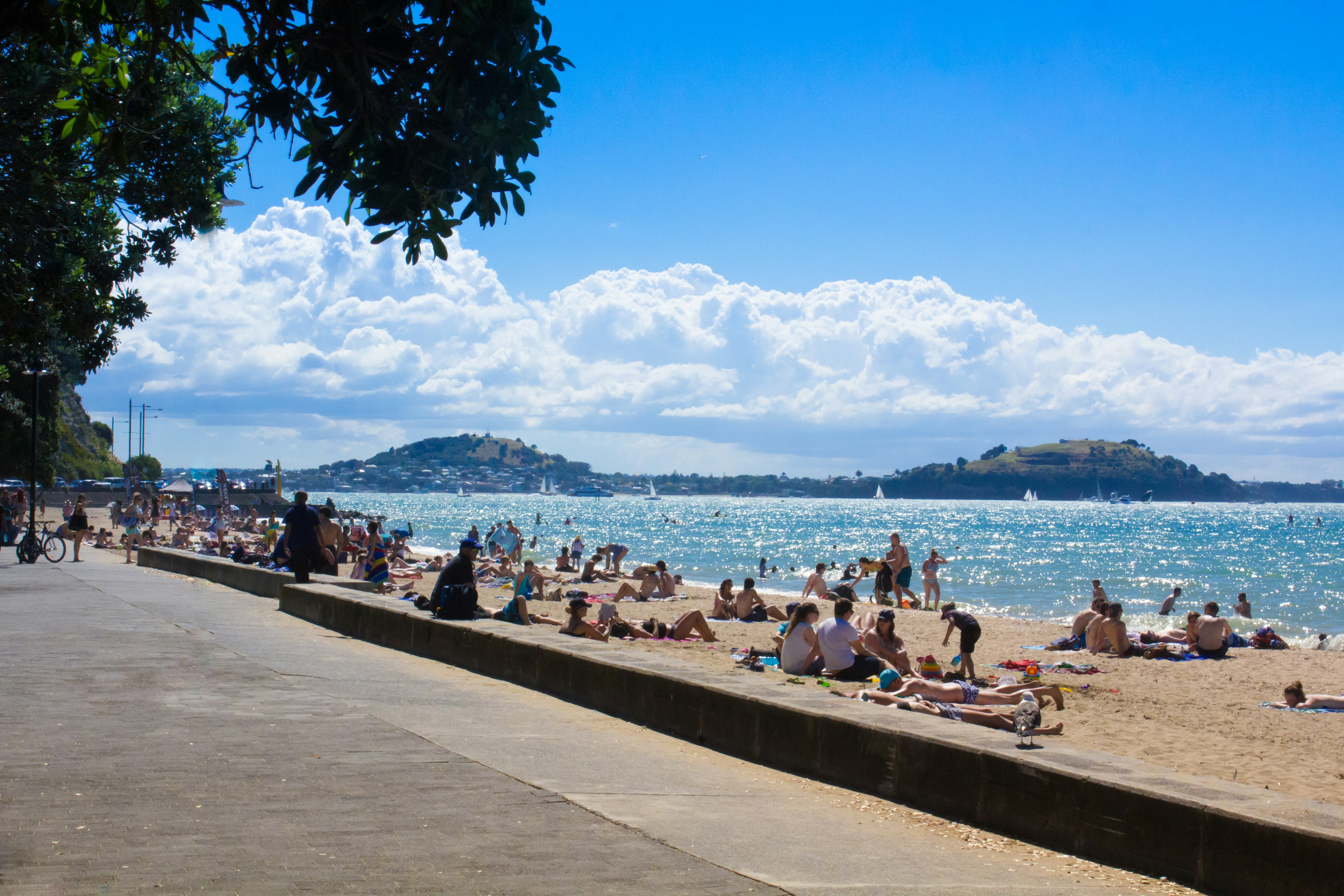 Escena de playa bajo un cielo azul con nubes blancas personas tomando el sol y islas cercanas visibles