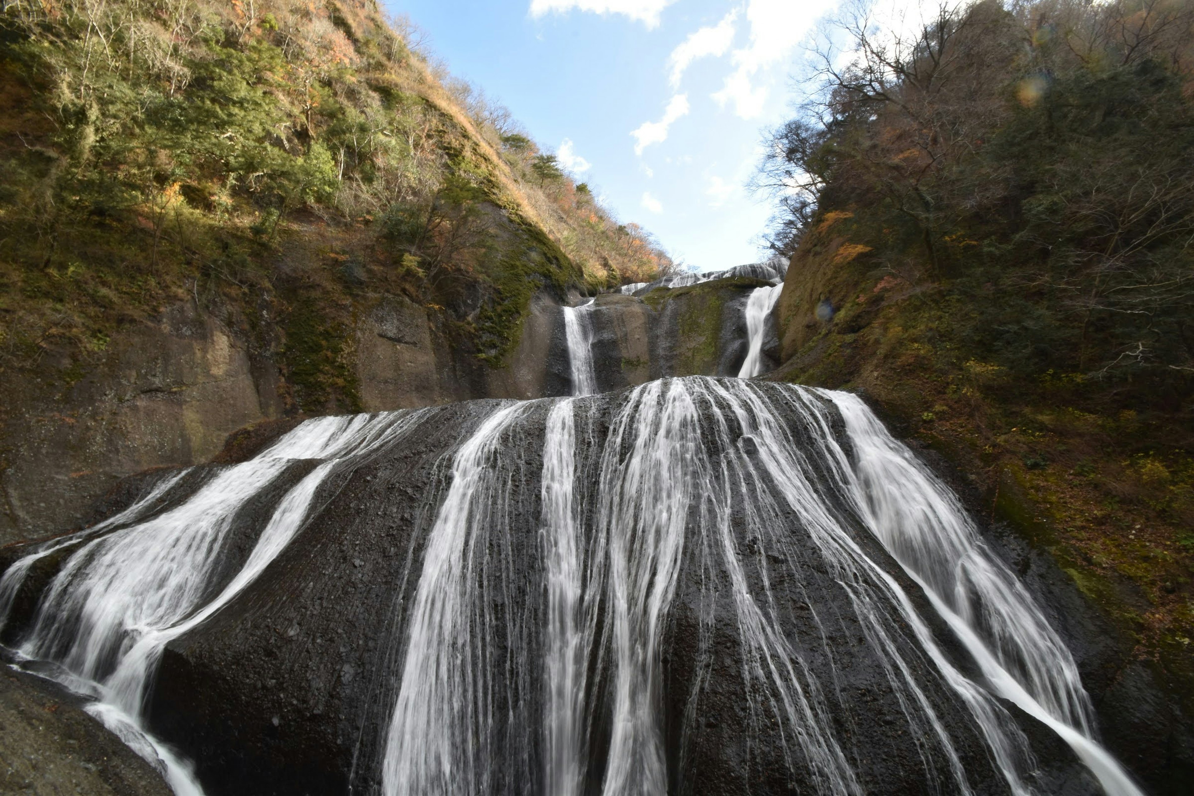 Una vista panoramica di una bellissima cascata che scorre su un terreno roccioso con colline verdi e cielo blu