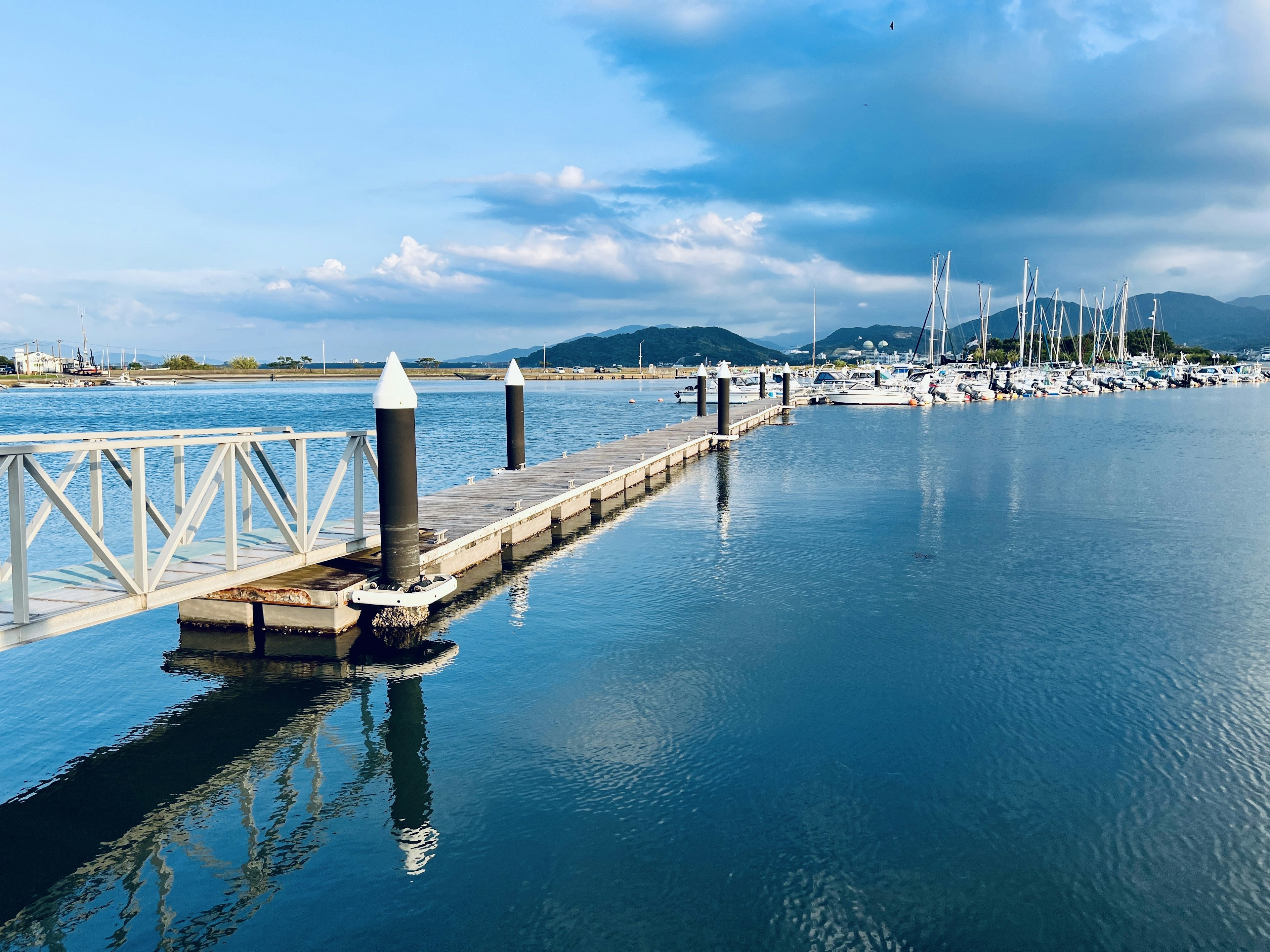 Jembatan kayu yang membentang di atas air tenang dengan perahu di latar belakang