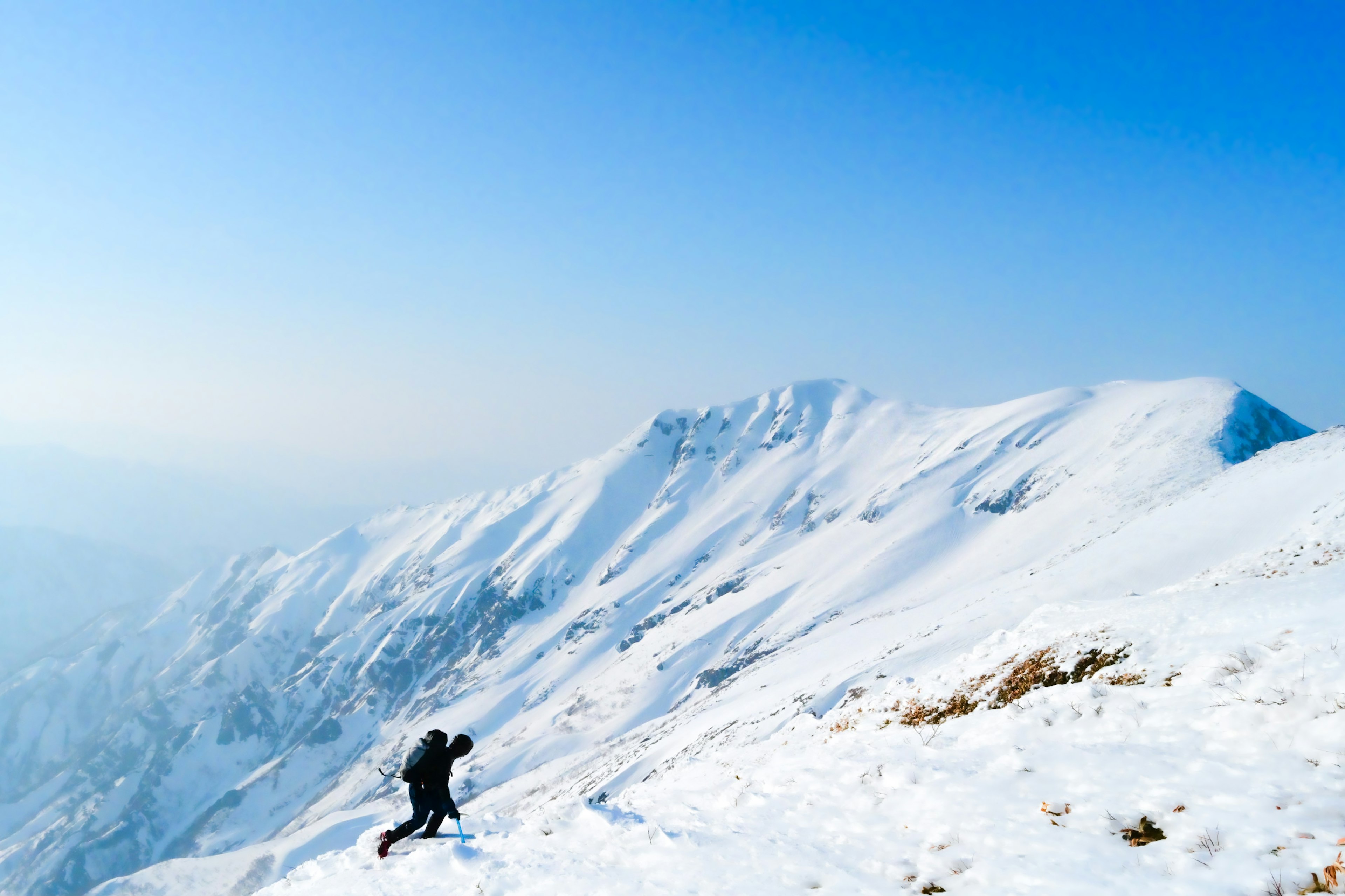 Escursionista che sale una montagna innevata sotto un cielo blu chiaro