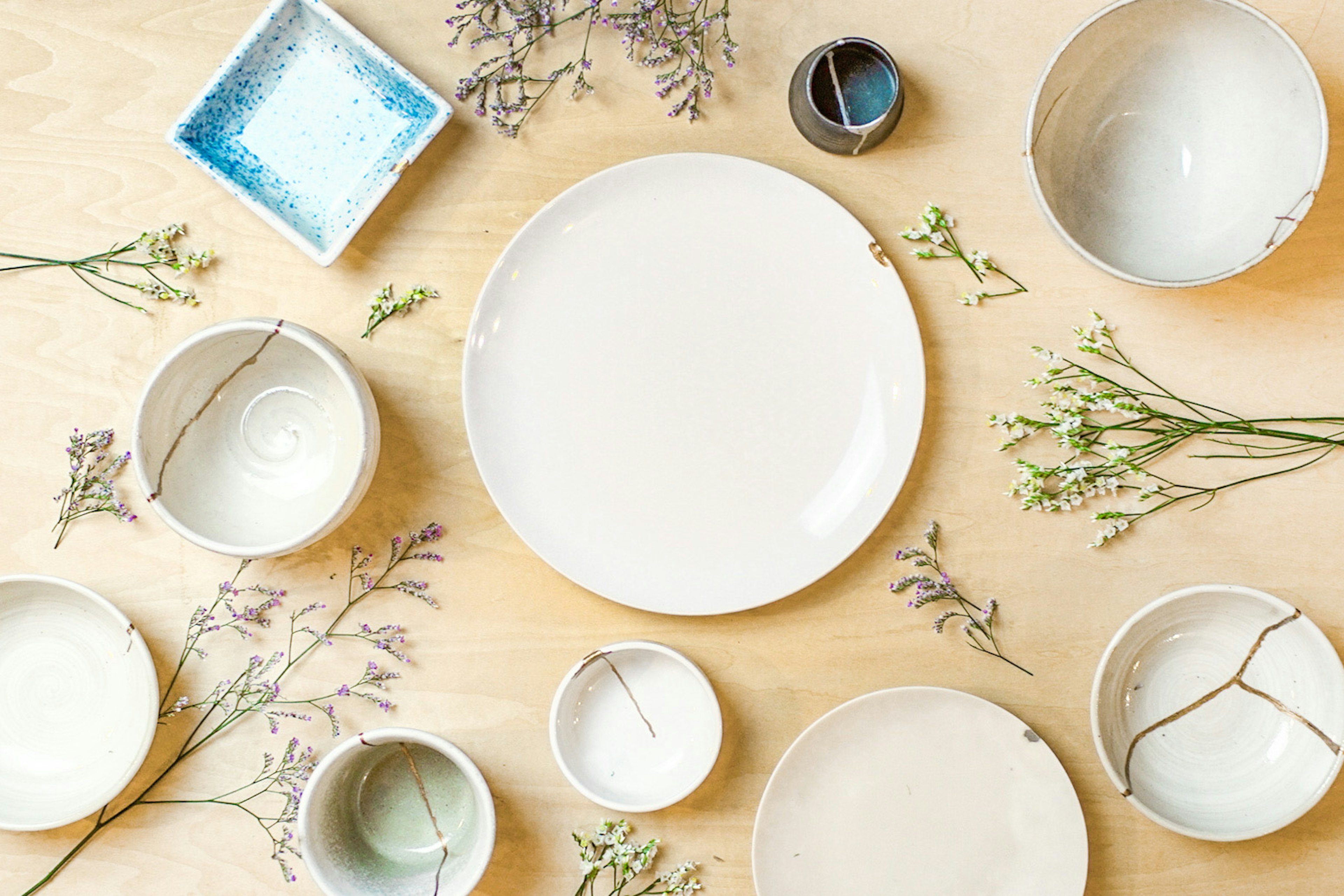 An arrangement of white plates and bowls on a wooden table surrounded by sprigs of greenery