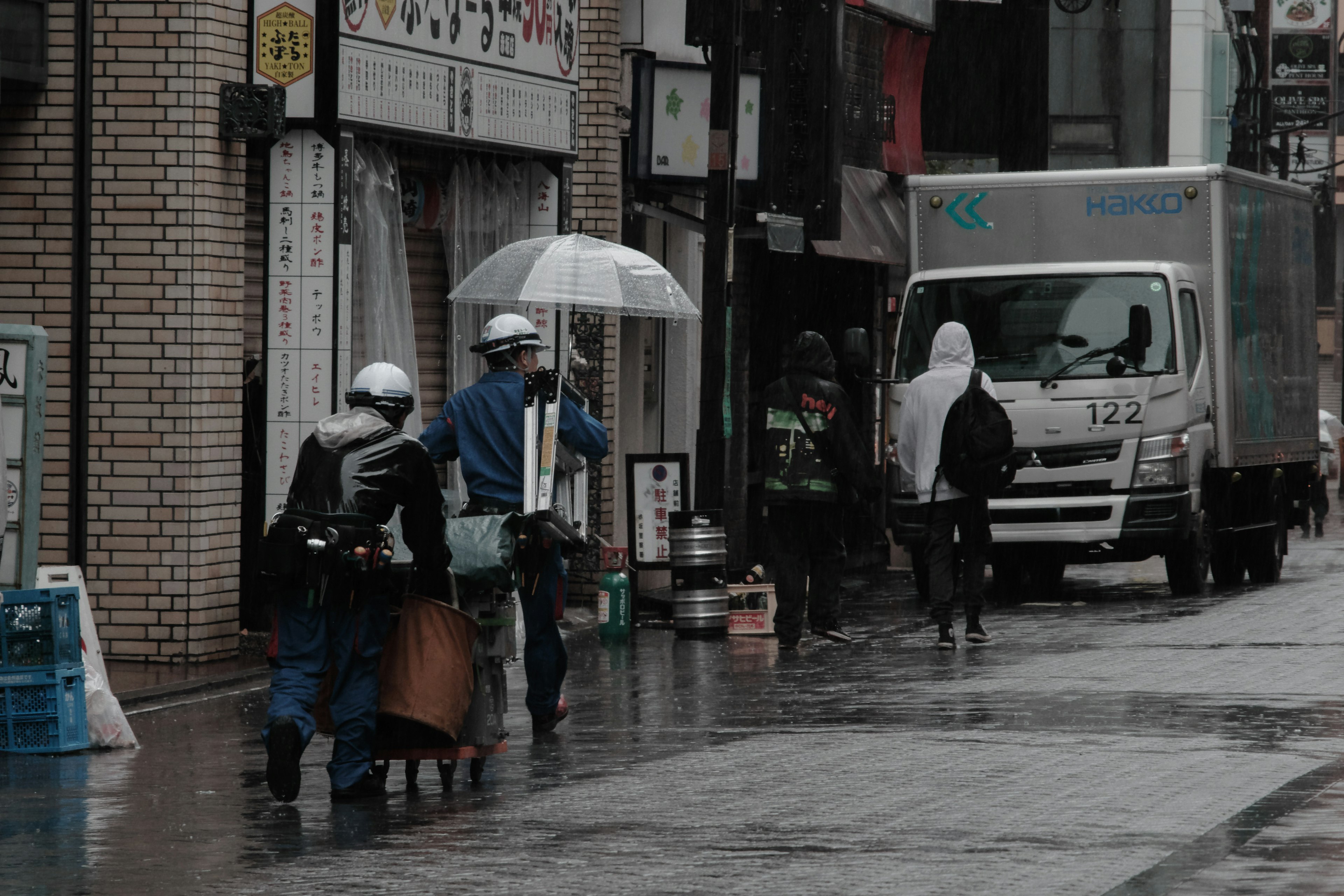 雨の中で傘を持つ作業員が通りを歩く風景