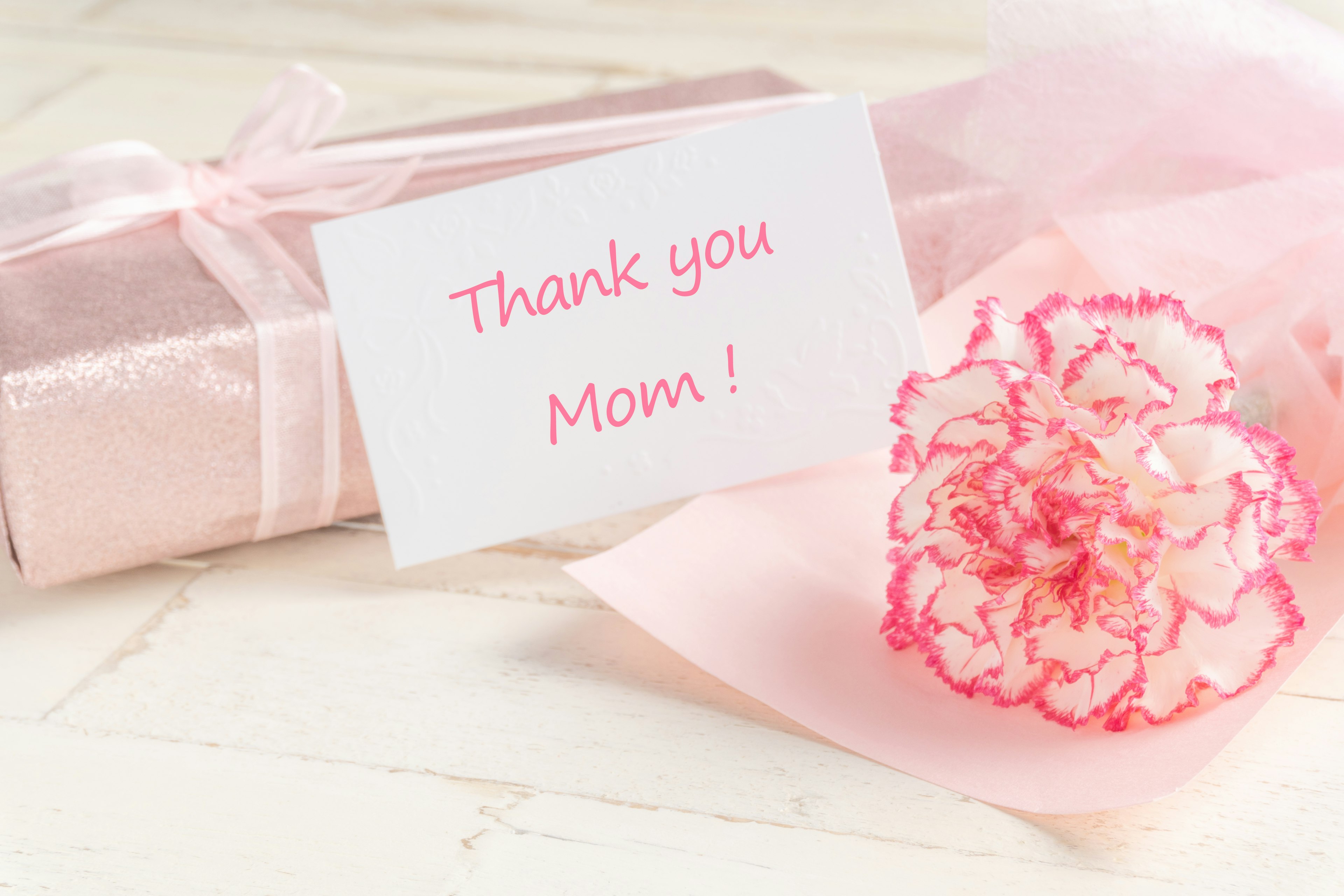 A pink-wrapped gift with a carnation flower and a message card saying Thank you Mom