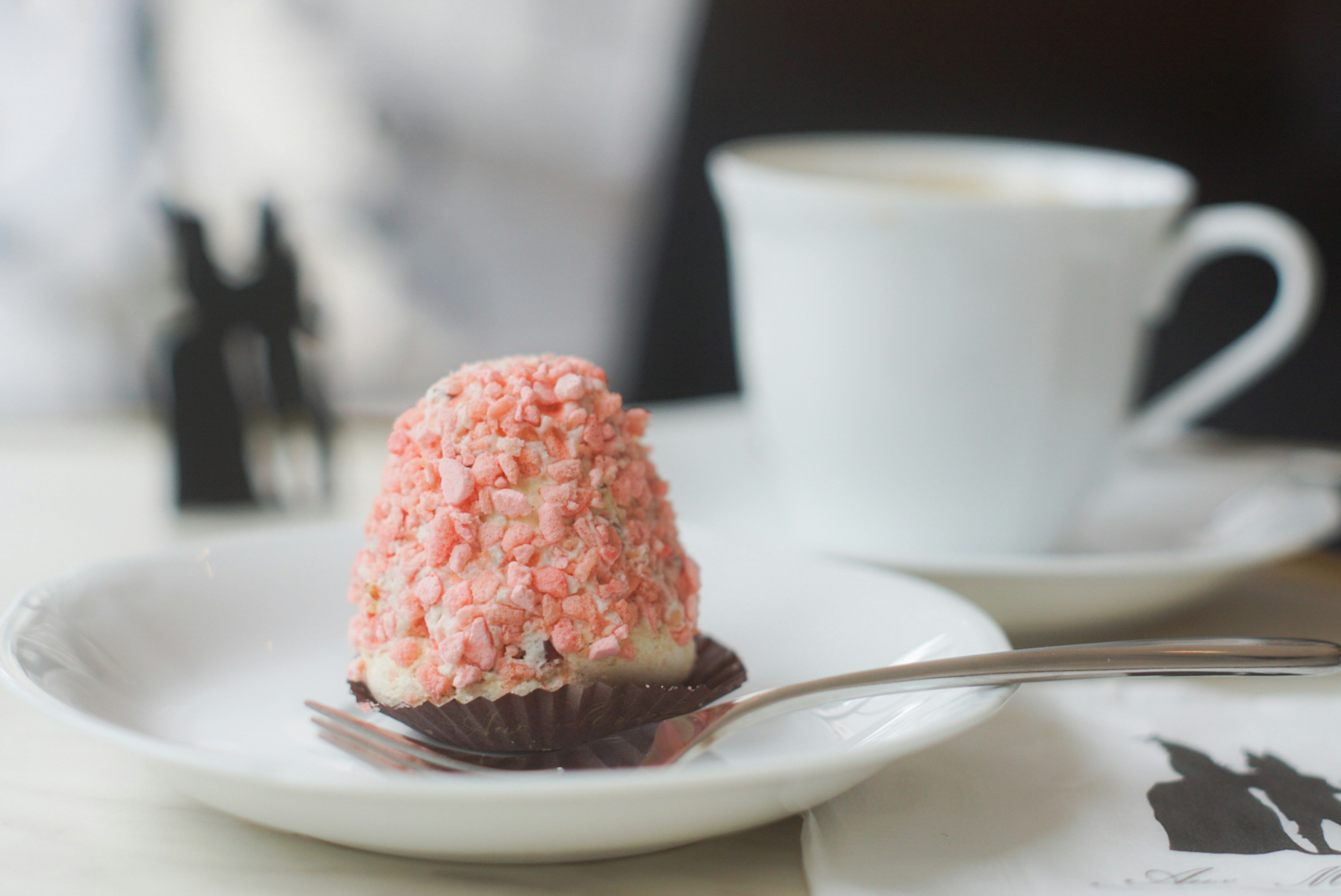 A cafe table featuring a coffee cup and a small pink dessert