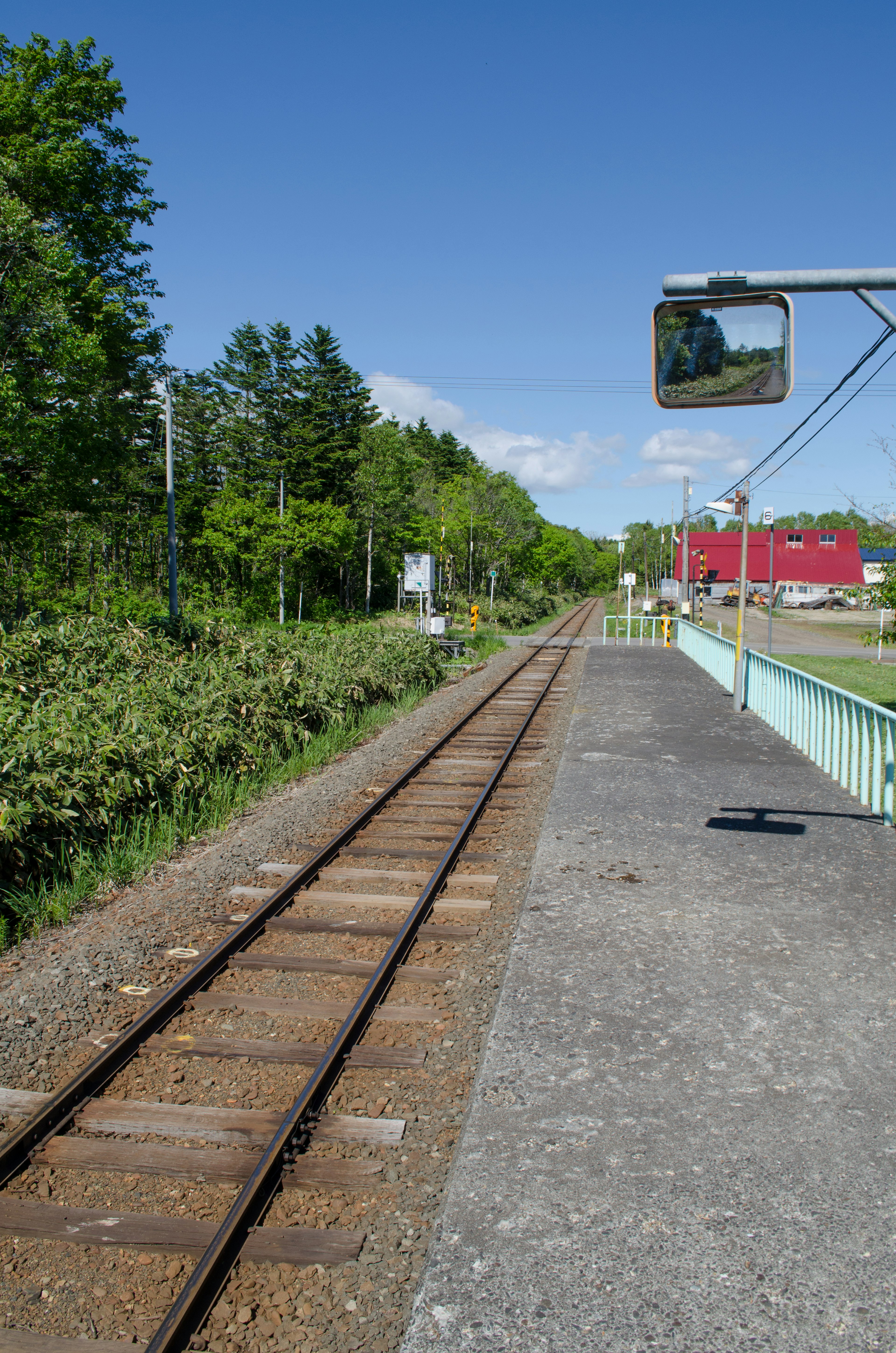 Plateforme de train avec des rails sous un ciel bleu arbres verts et un bâtiment rouge en arrière-plan