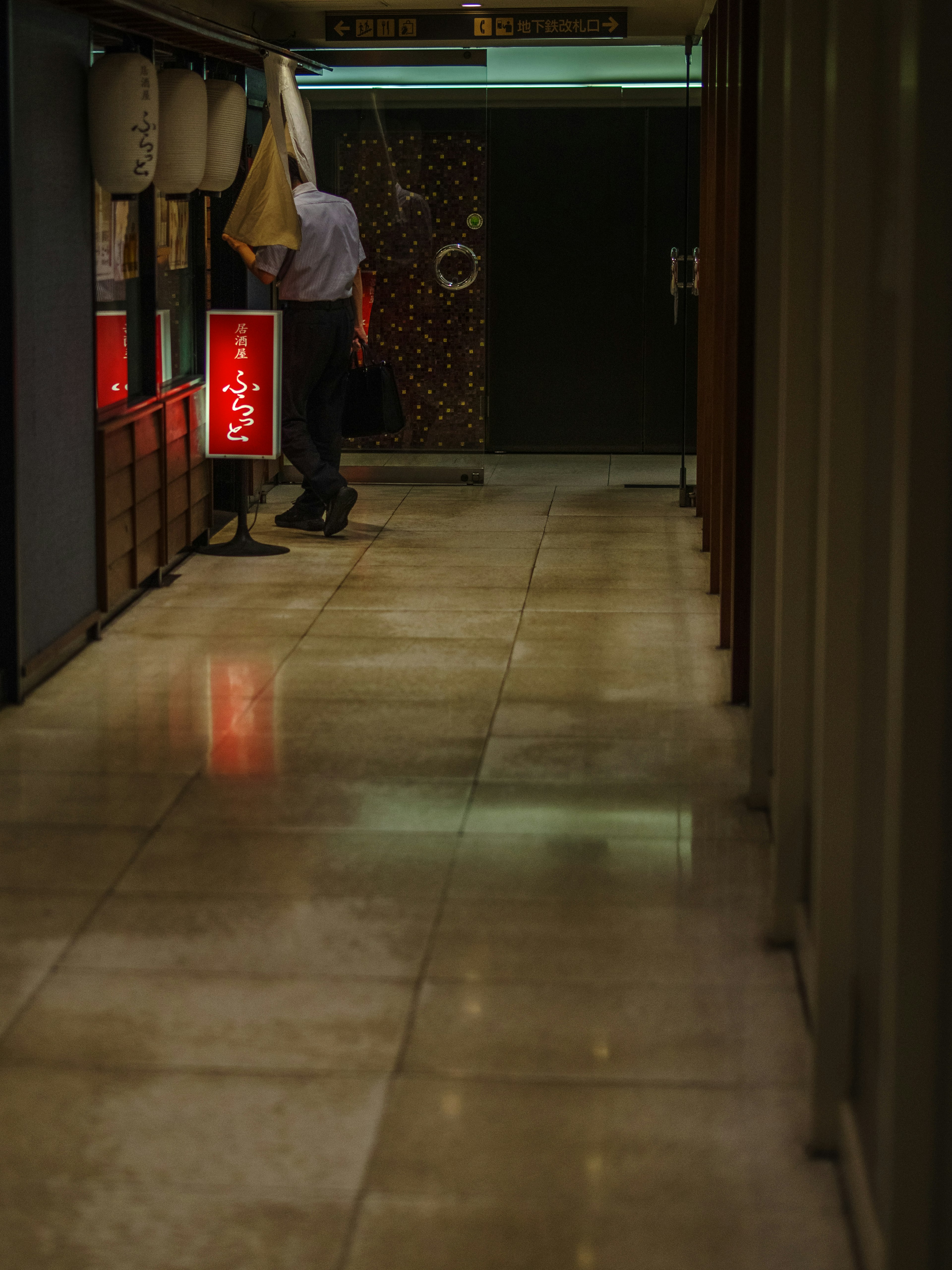 Eine Person steht vor einem traditionellen japanischen Geschäft mit roter Beschilderung in einem schwach beleuchteten Flur