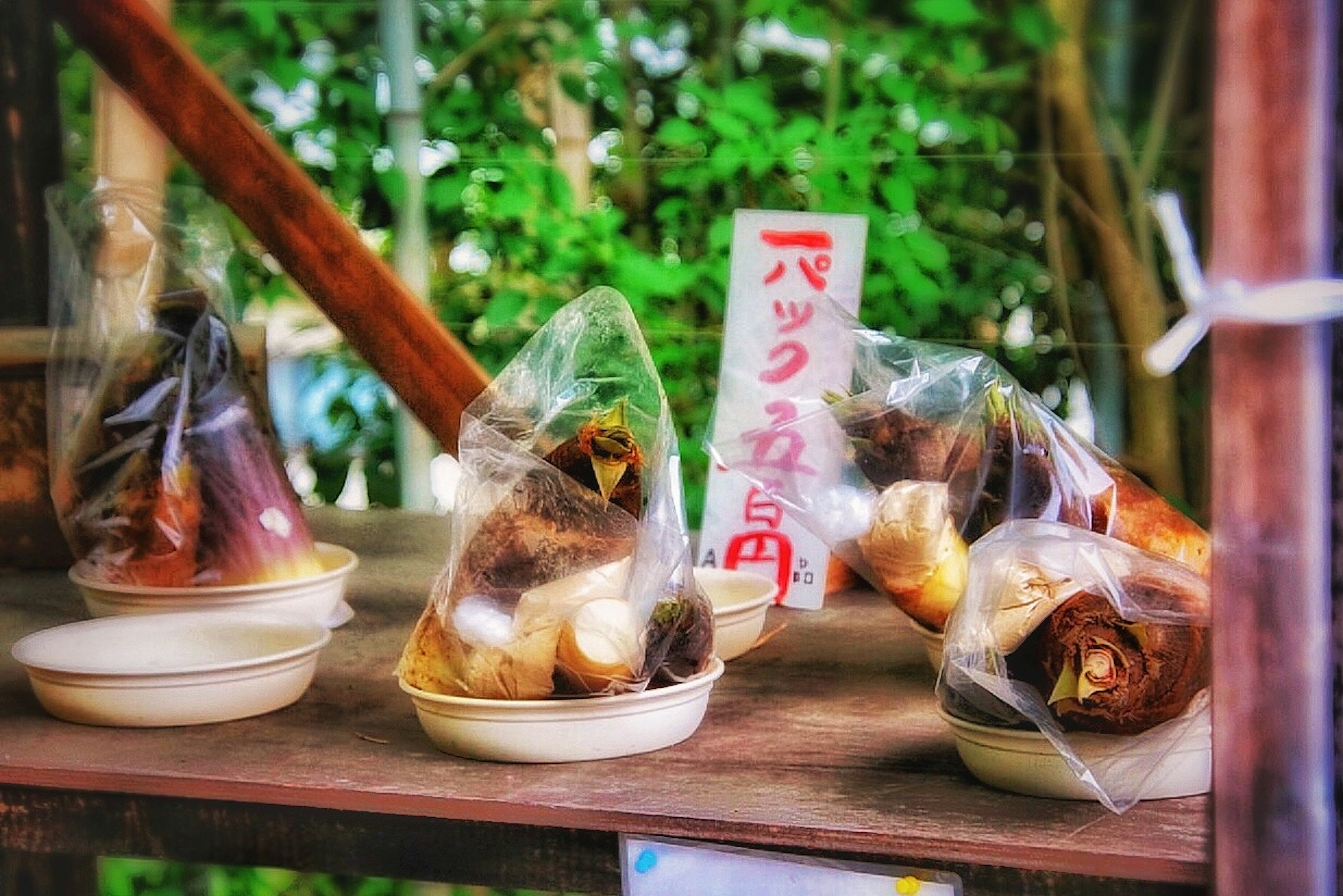 Packaged food items displayed on an outdoor shelf with green foliage in the background