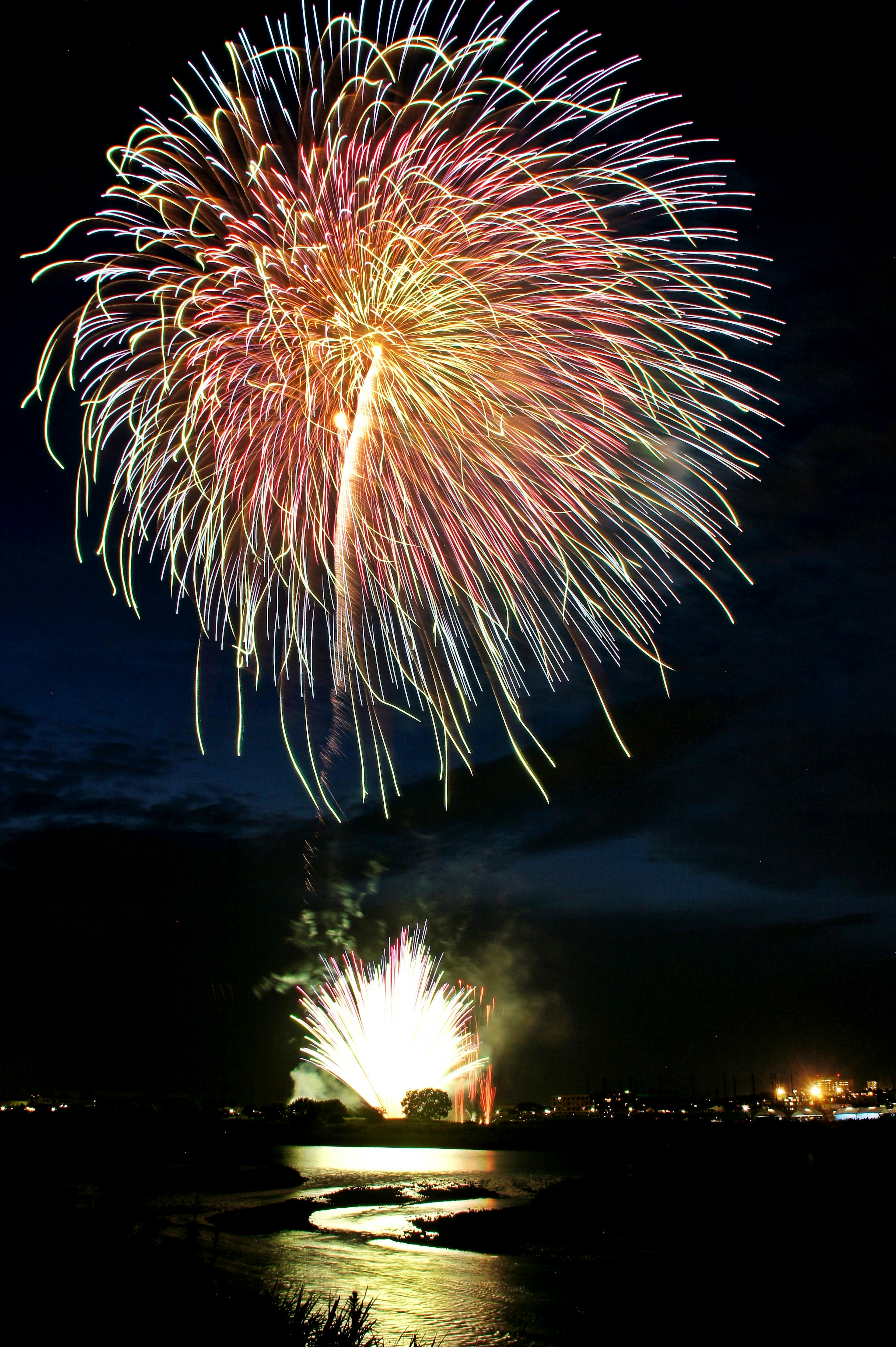 Un vivace spettacolo di fuochi d'artificio che illumina il cielo notturno con riflessi sull'acqua