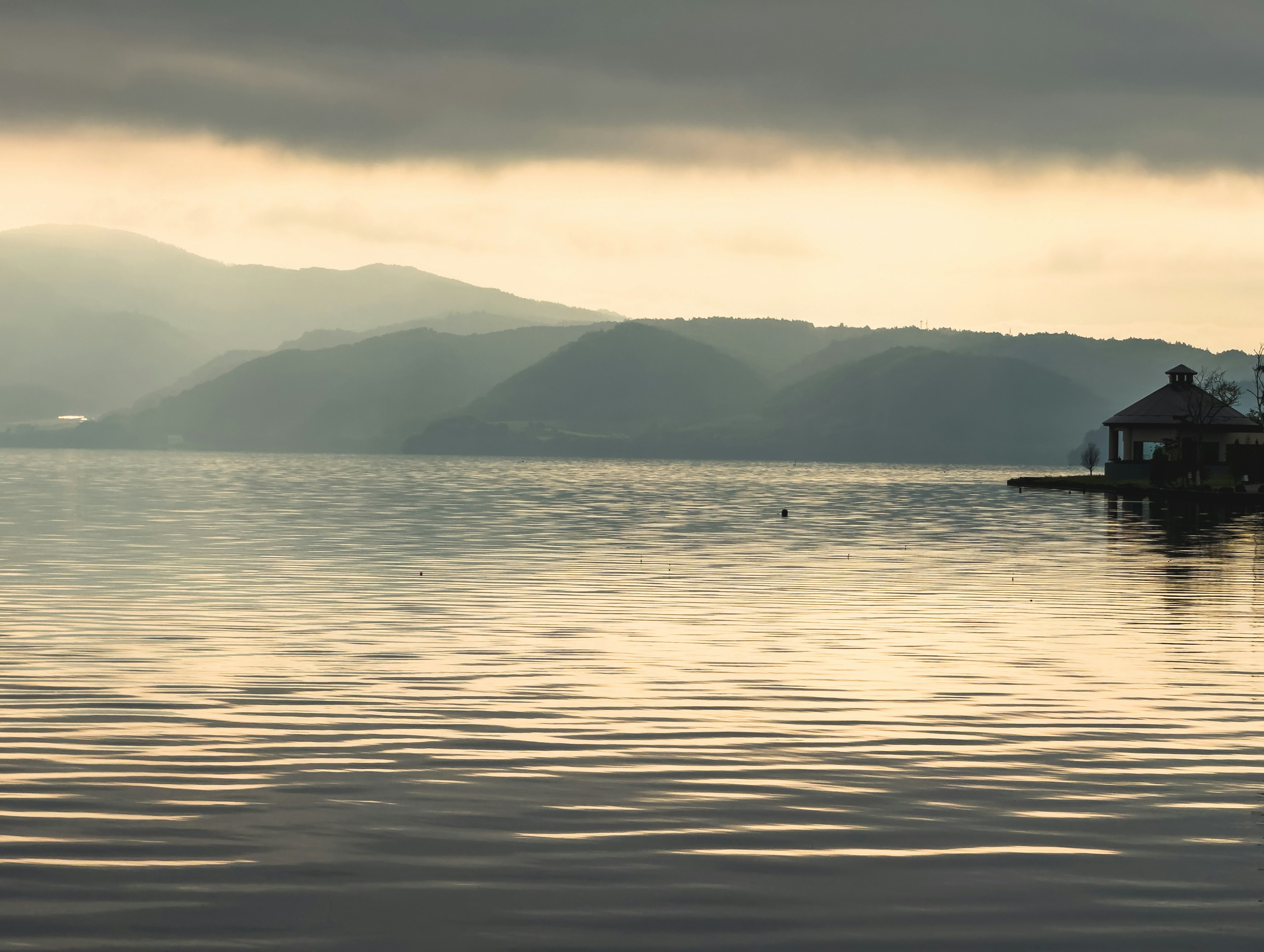 Pemandangan danau tenang dengan pegunungan dan langit mendung