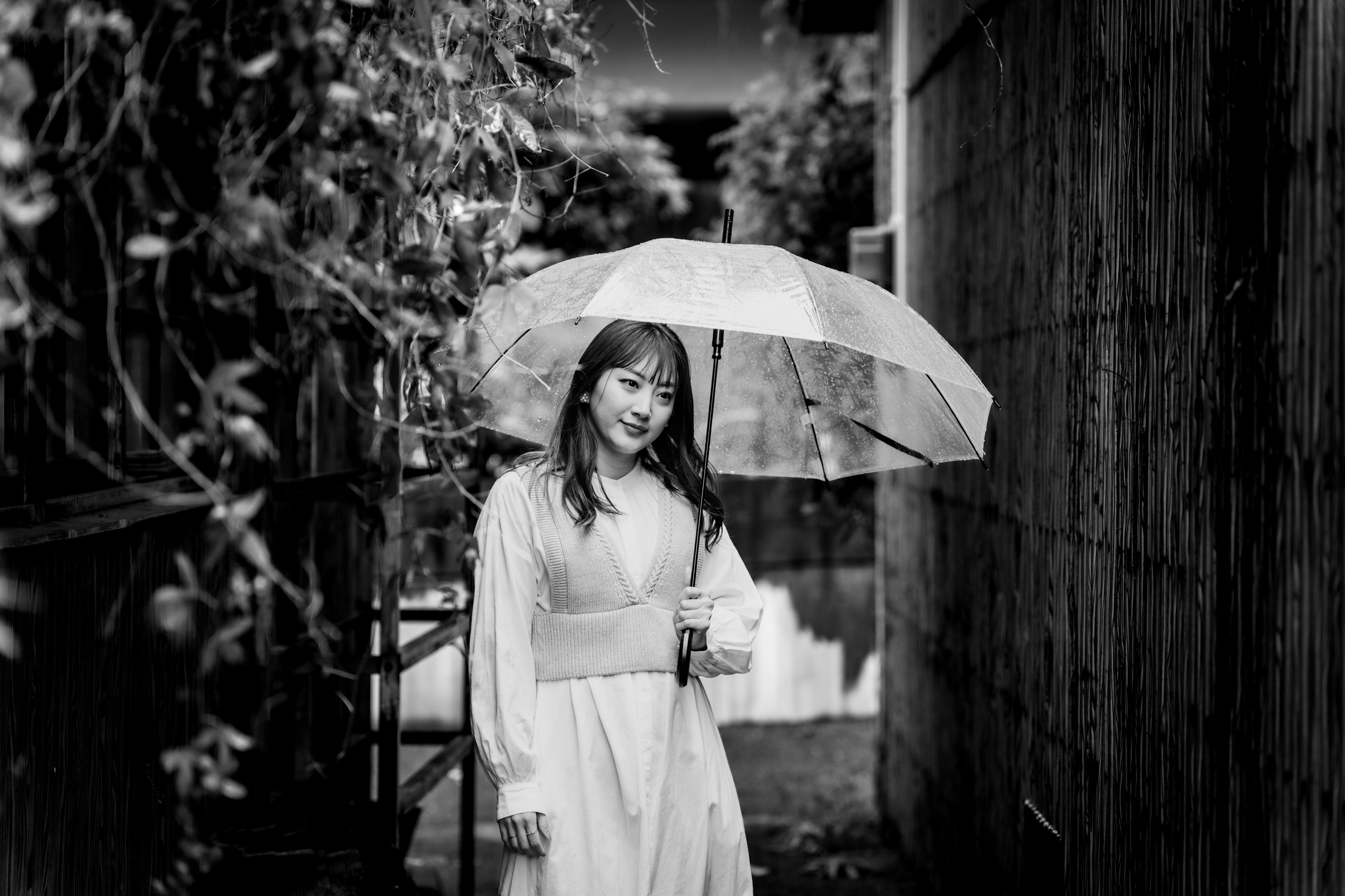 A woman in a white dress holding a transparent umbrella in a black and white photo