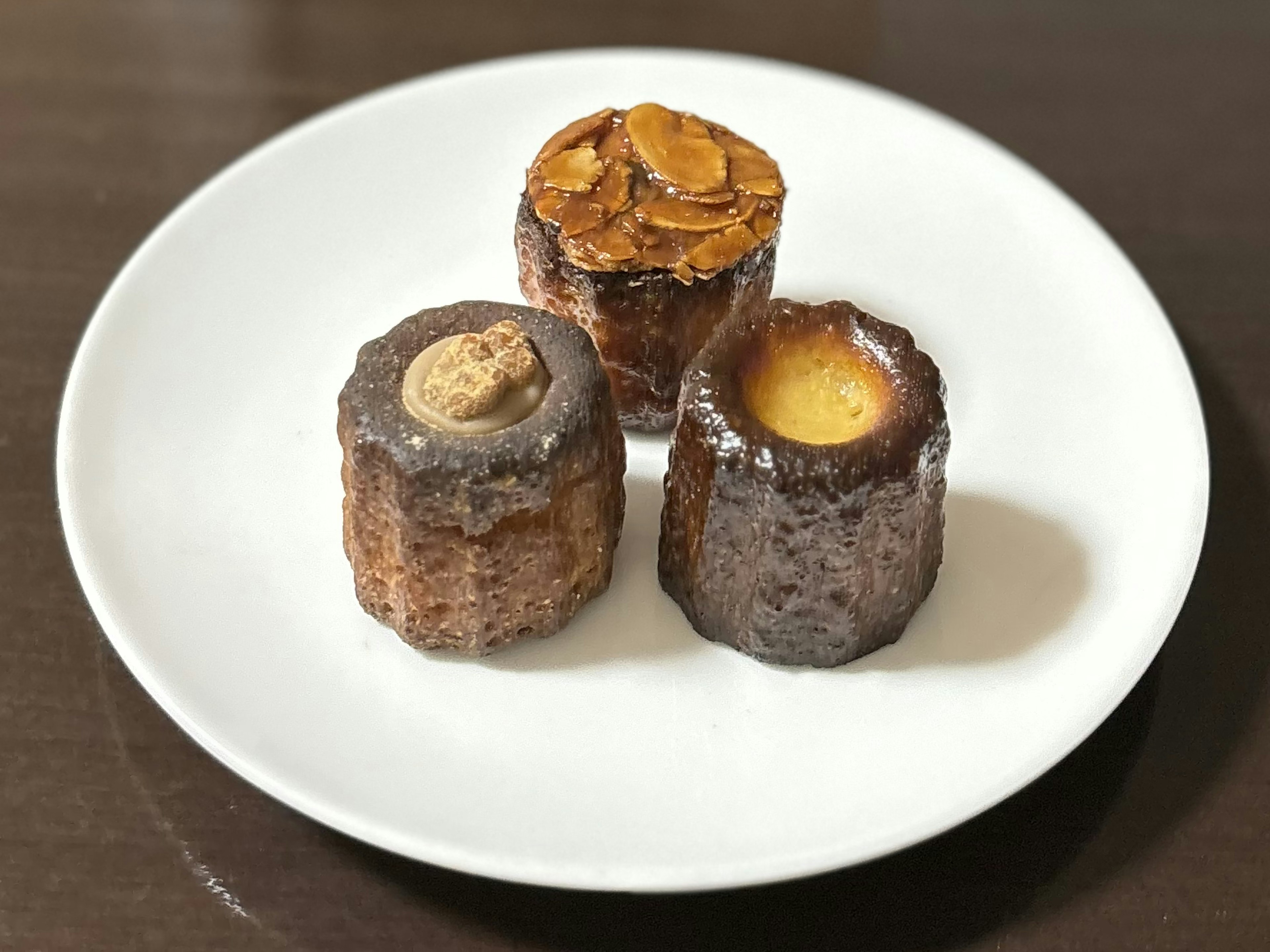 Three baked goods on a white plate featuring one with almond topping and others with creamy textures