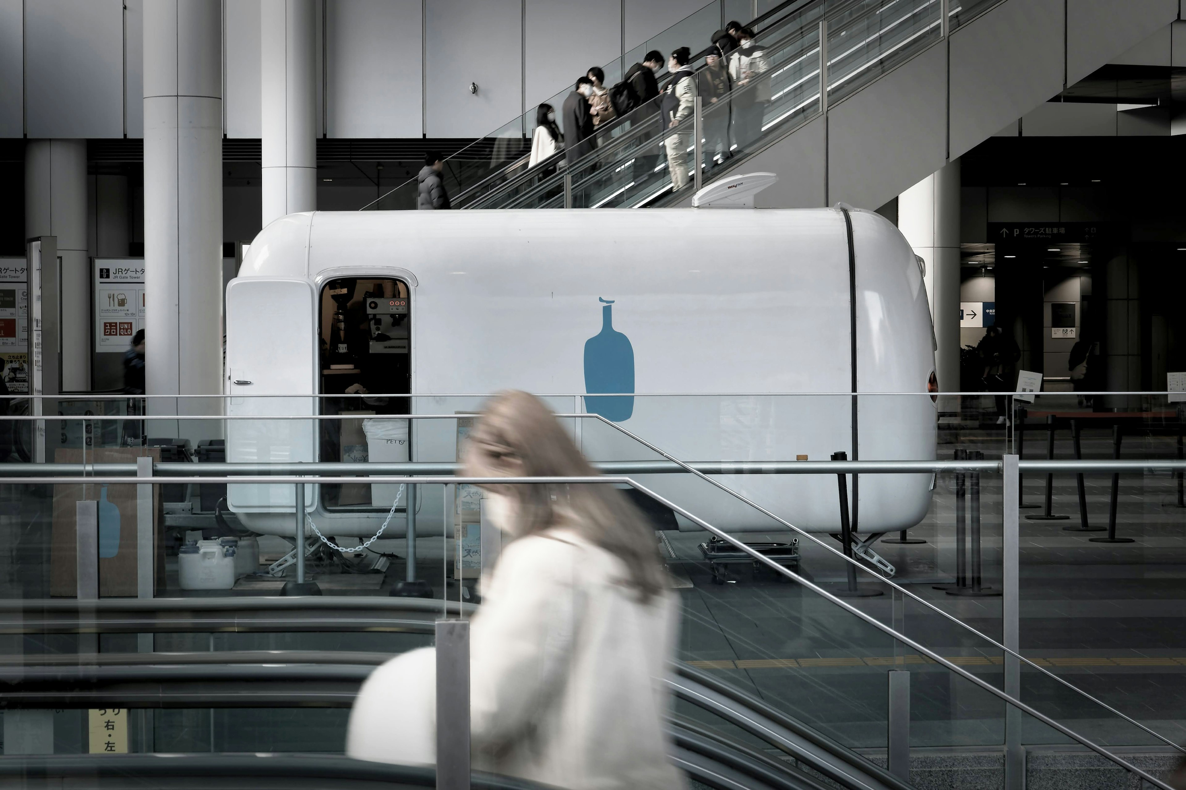 Remorque blanche avec logo de bouteille bleue dans un espace commercial avec des gens en mouvement