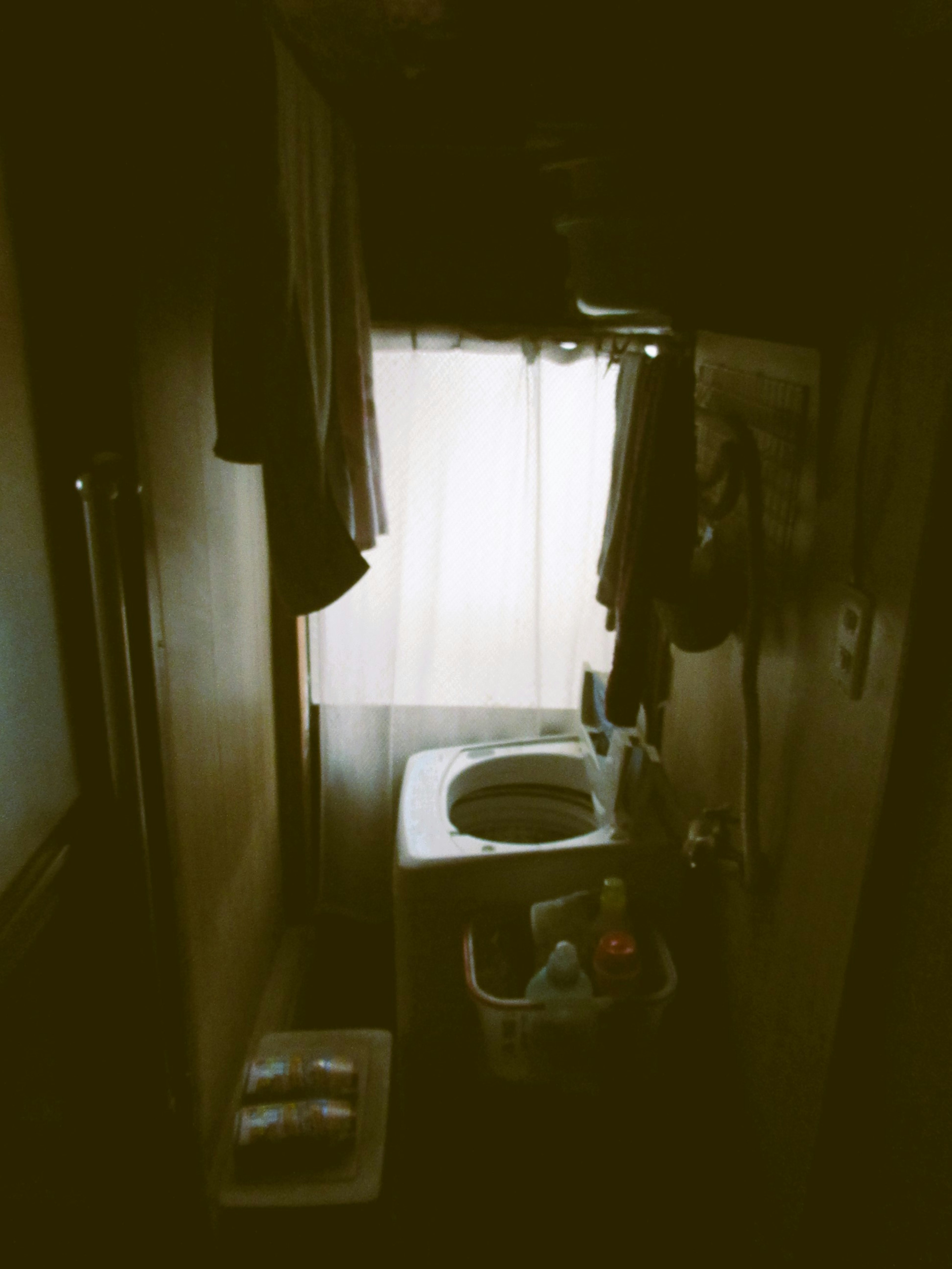 Narrow laundry room with a window and a washing machine surrounded by hanging clothes