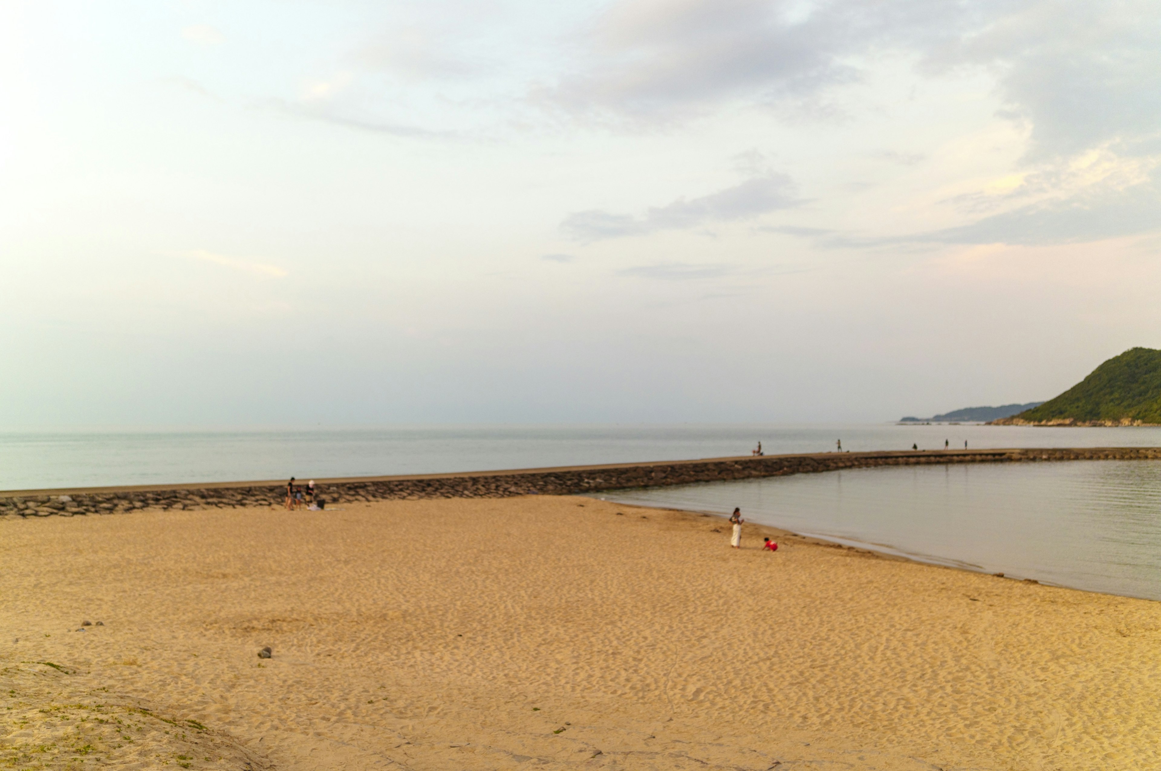 Pemandangan pantai dengan laut tenang dan tepi pasir saat senja