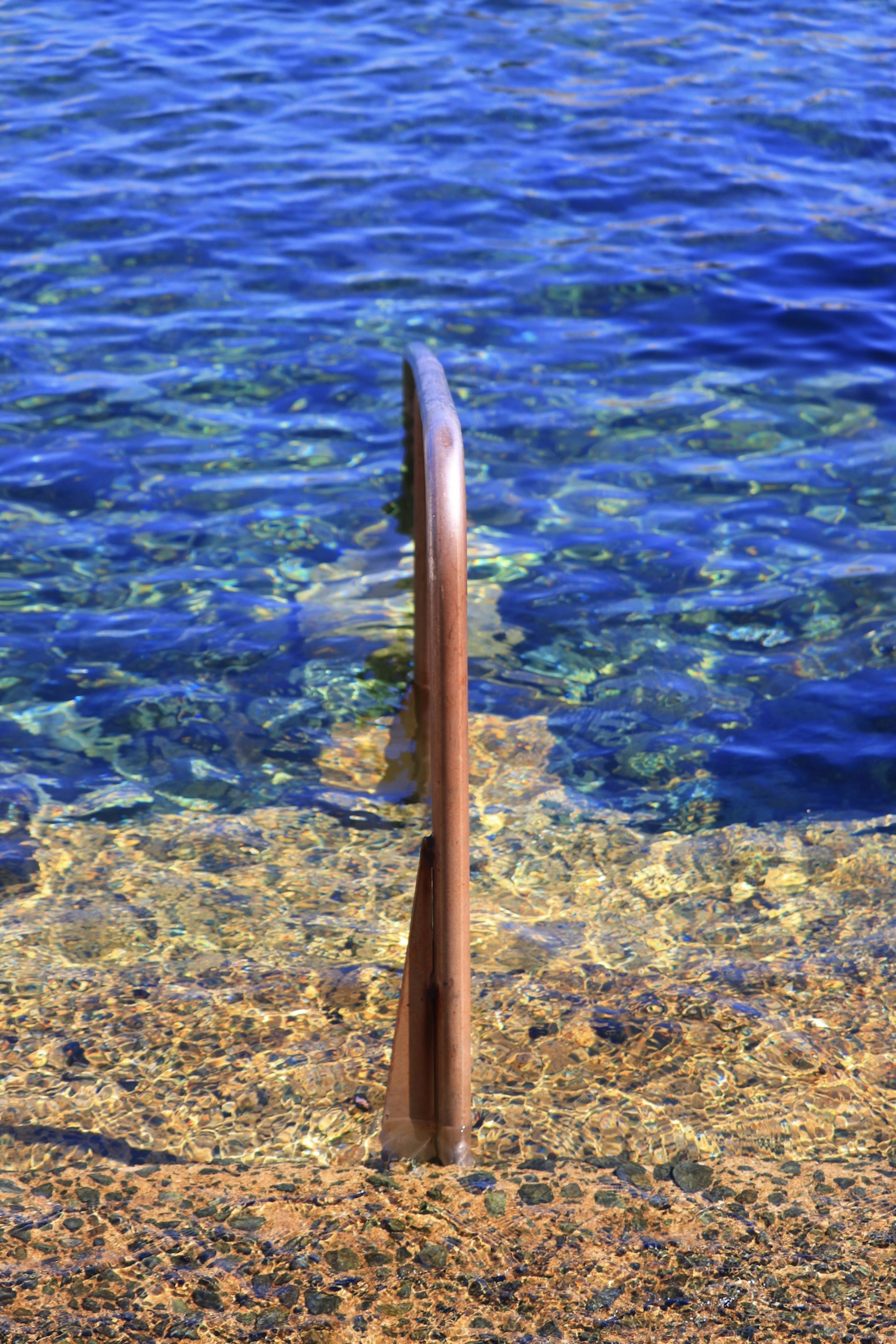 Metal railing above clear blue water with rocky shore