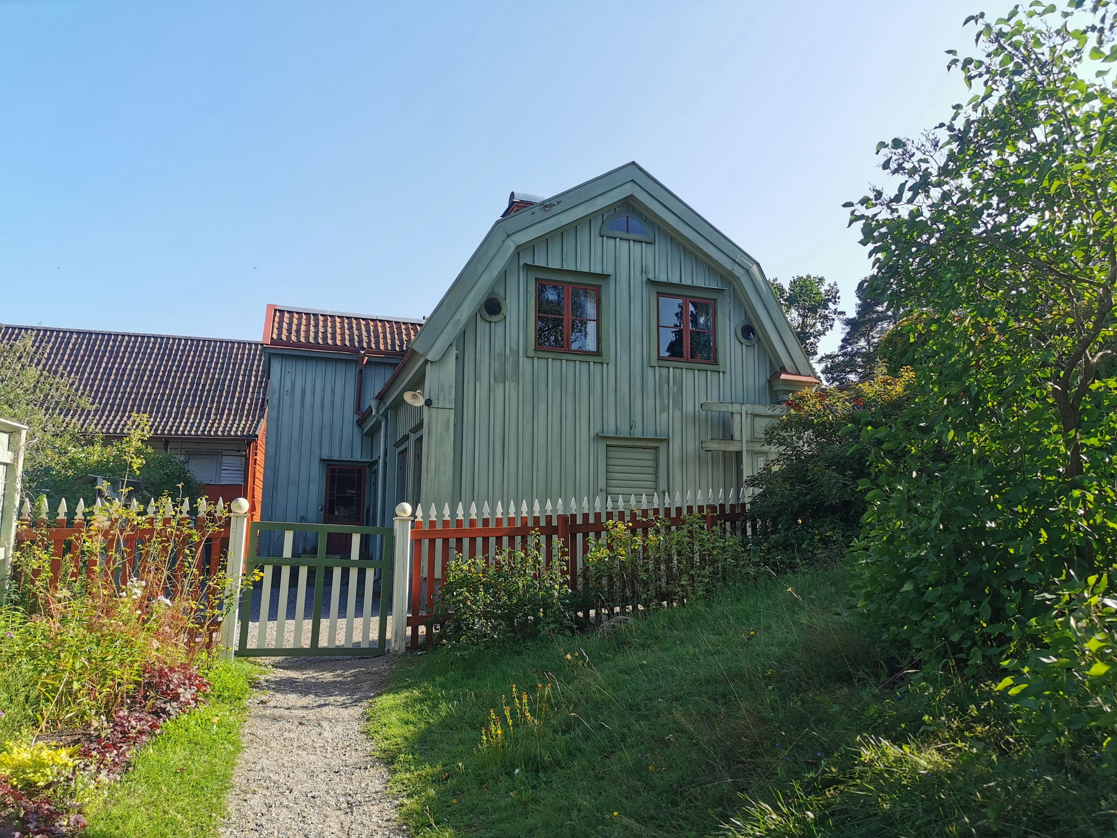 A green wooden house with a white picket fence and a garden