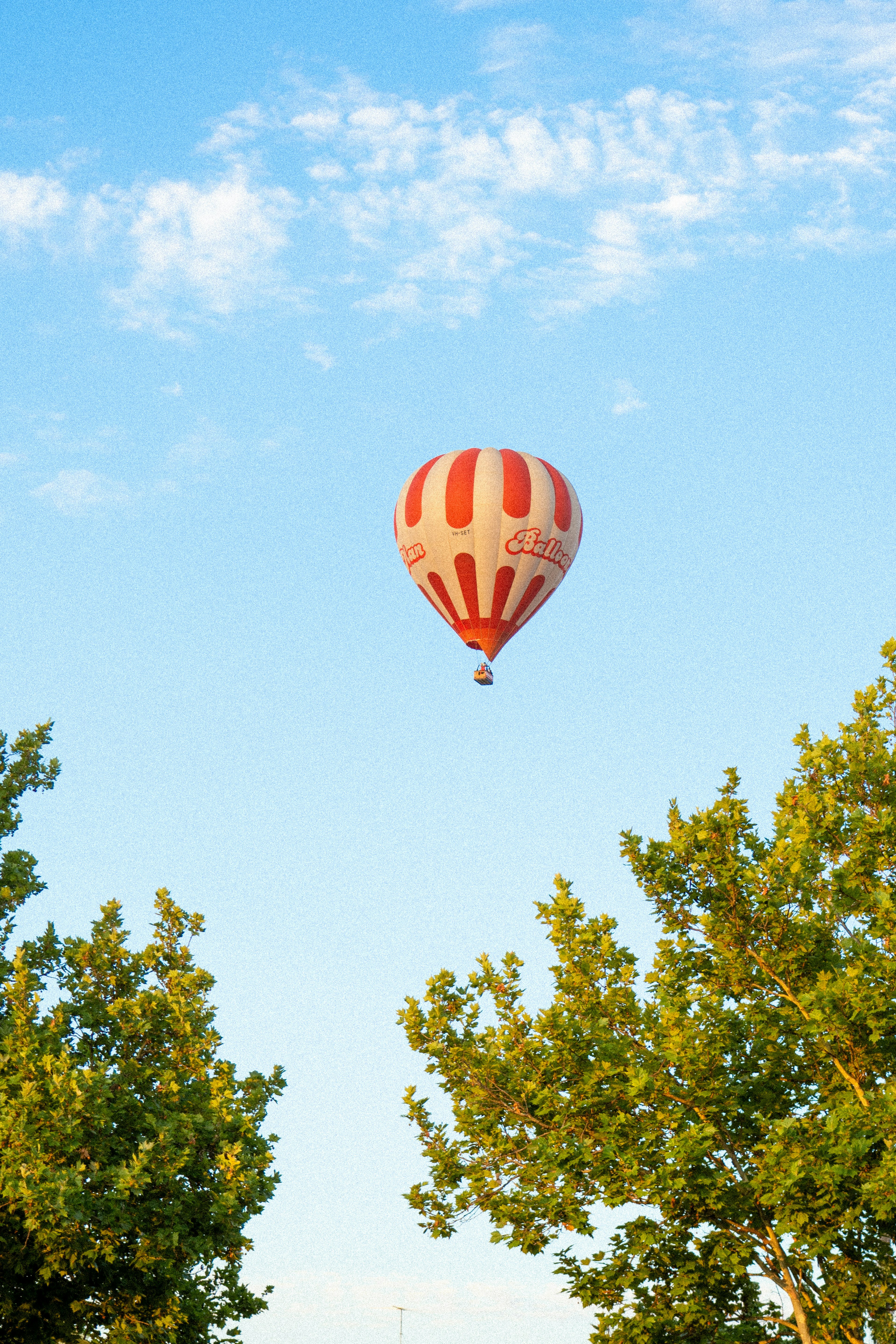 Red and white striped hot air balloon flying in the blue sky among trees