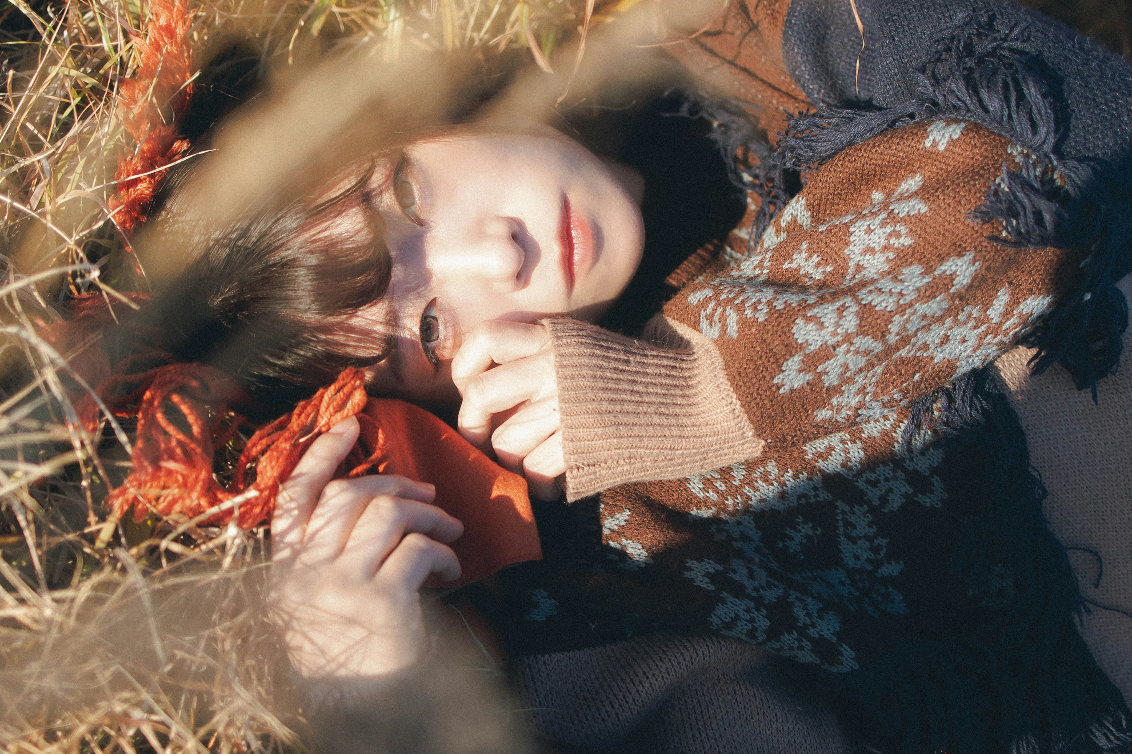 A woman lying in grass with closed eyes featuring an orange cloth and floral sweater