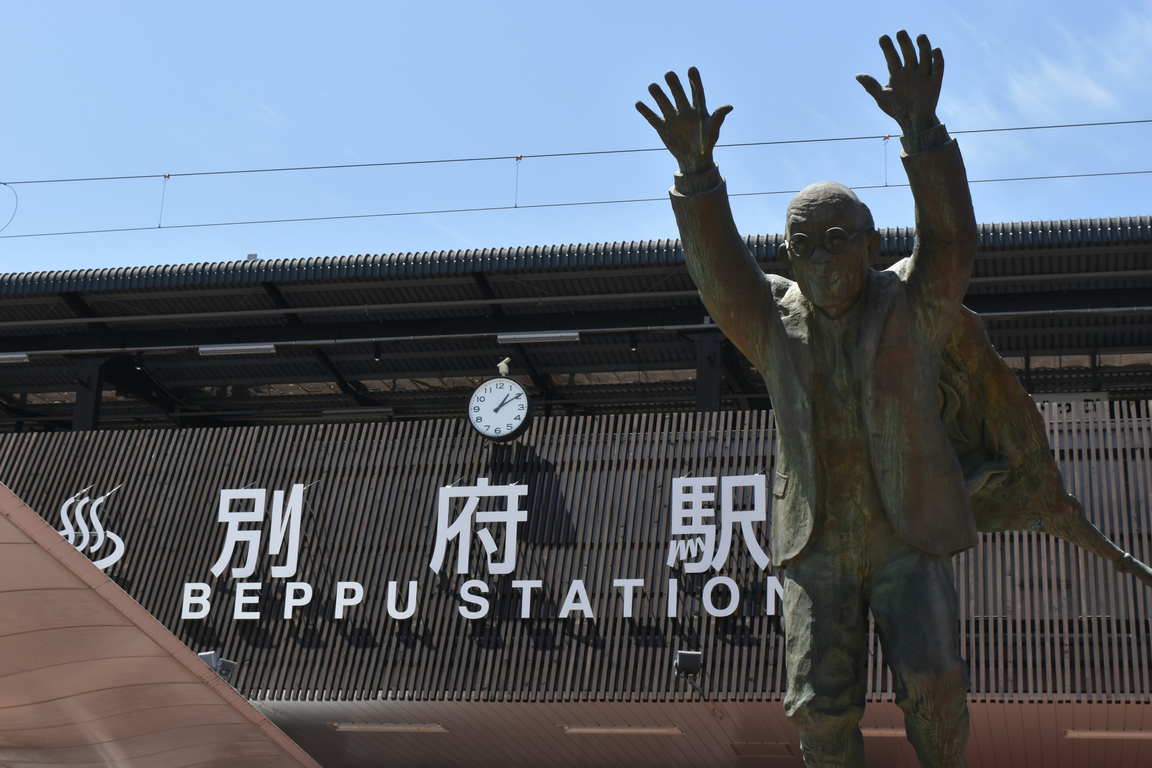 Statue in front of Beppu Station with clock and signage