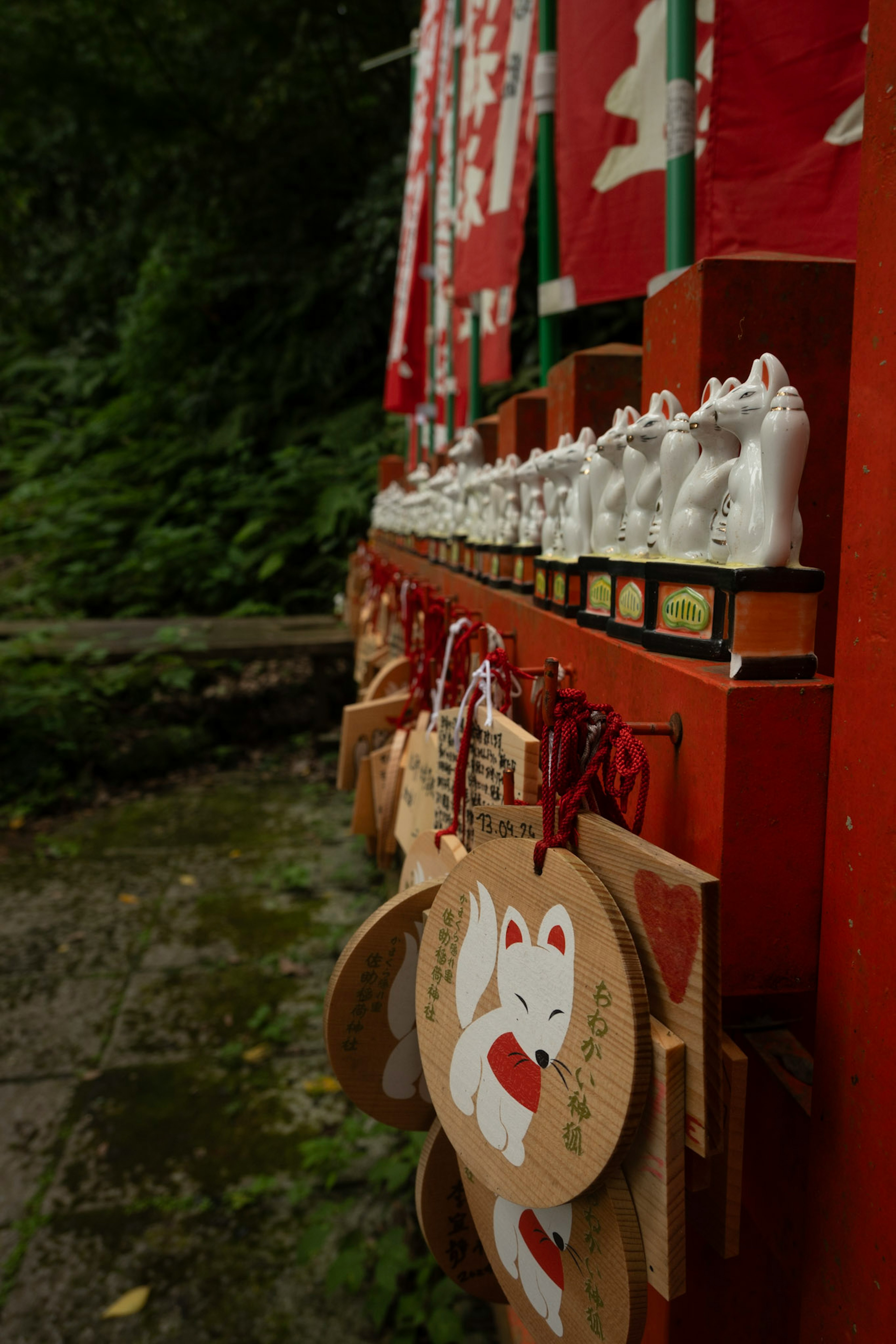 白い小さな狐の像と赤い絵馬が並ぶ神社の風景