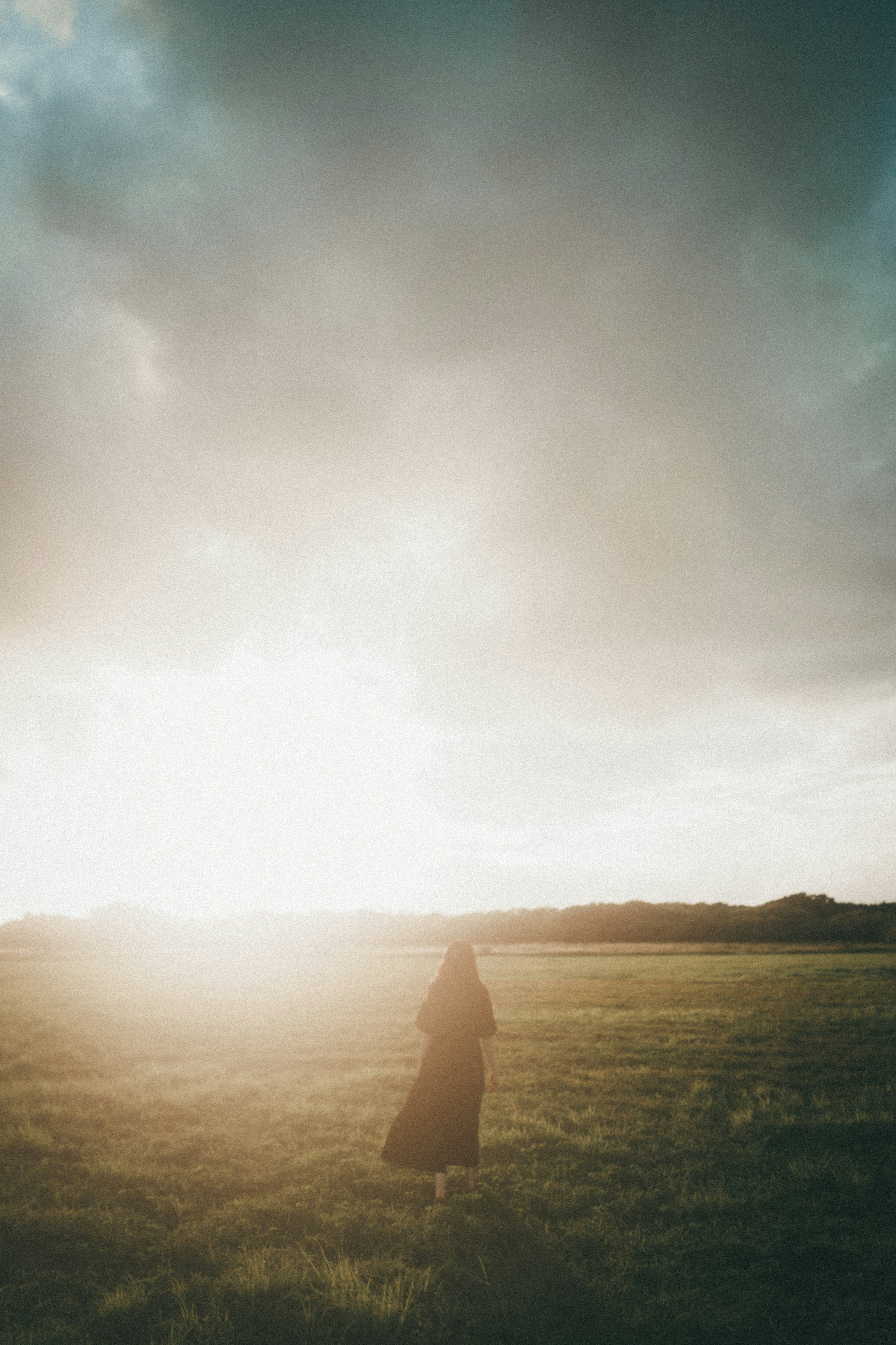 Une personne marchant dans une vaste prairie avec le coucher de soleil derrière elle