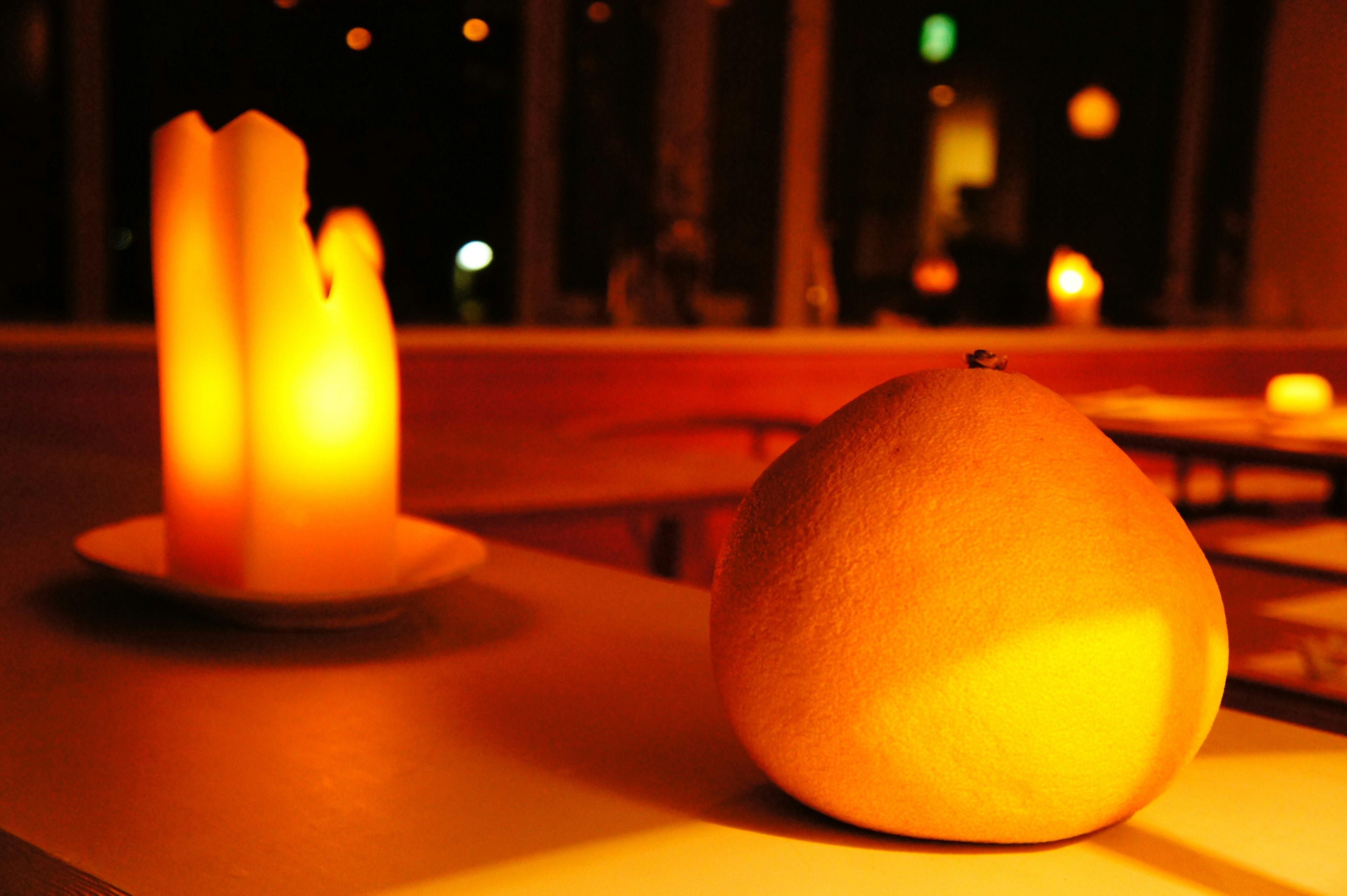 An orange fruit on a table with glowing candles in the background