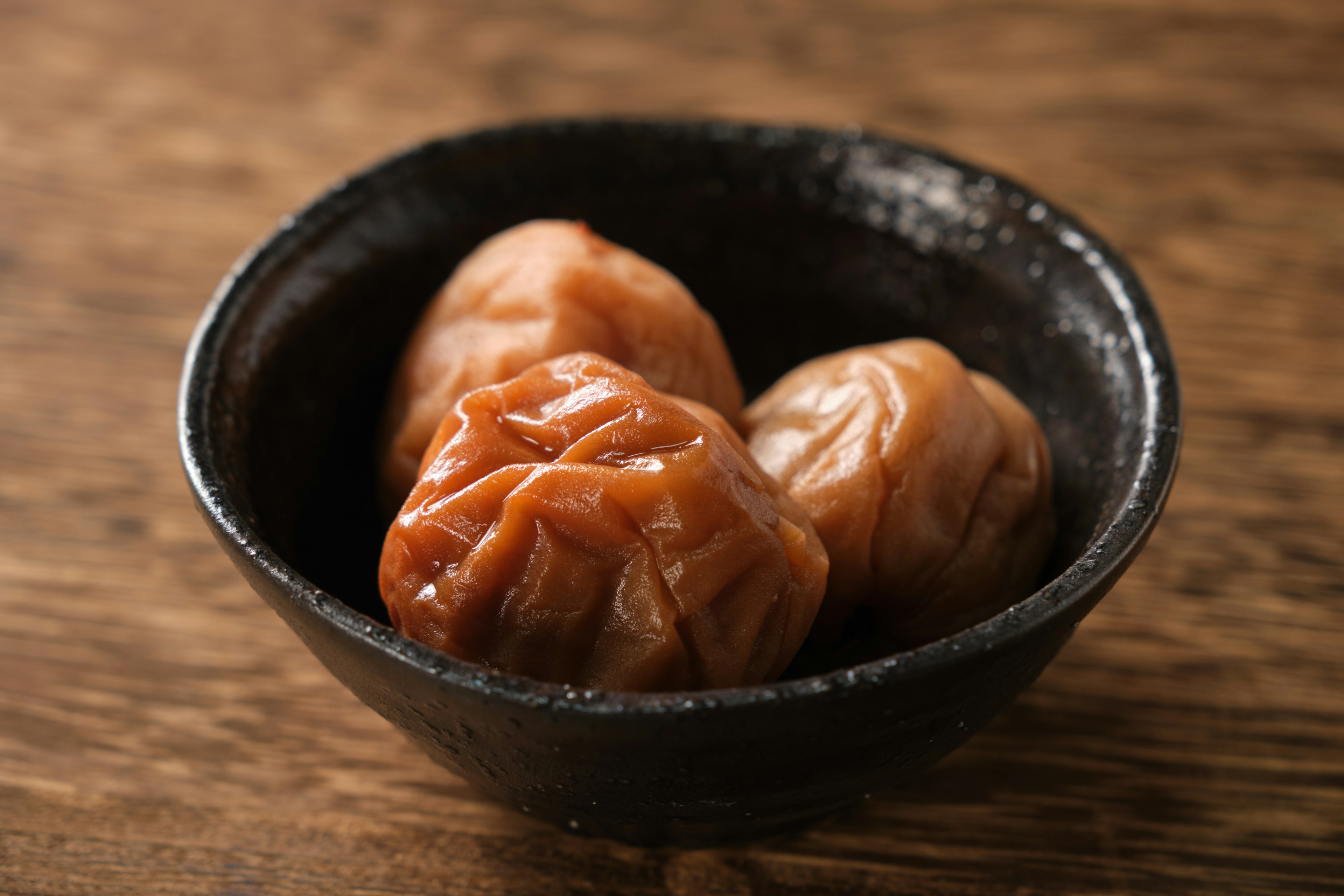 Image of pickled plums served in a black ceramic bowl