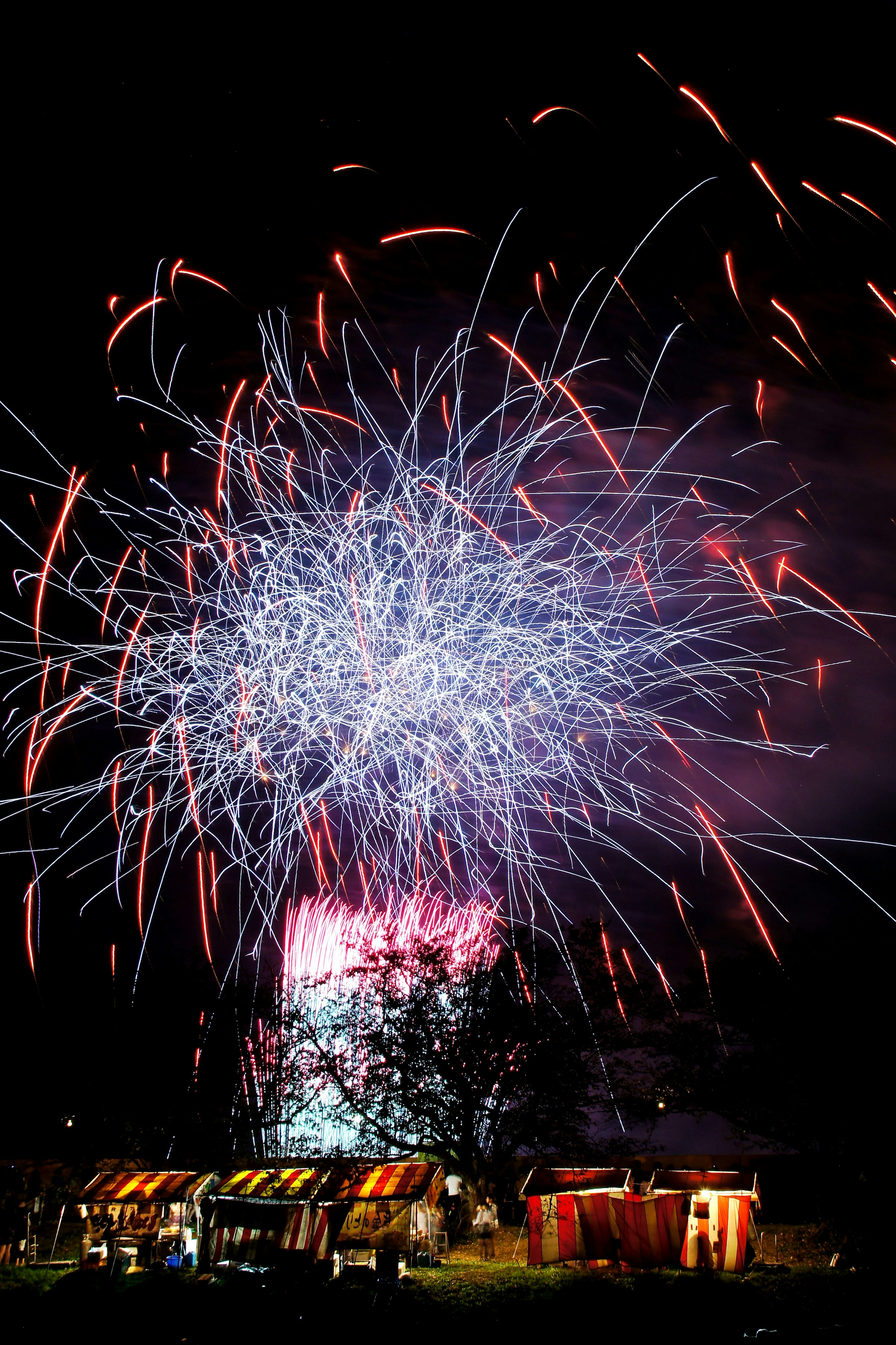 Fuegos artificiales coloridos estallando en el cielo nocturno con puestos abajo