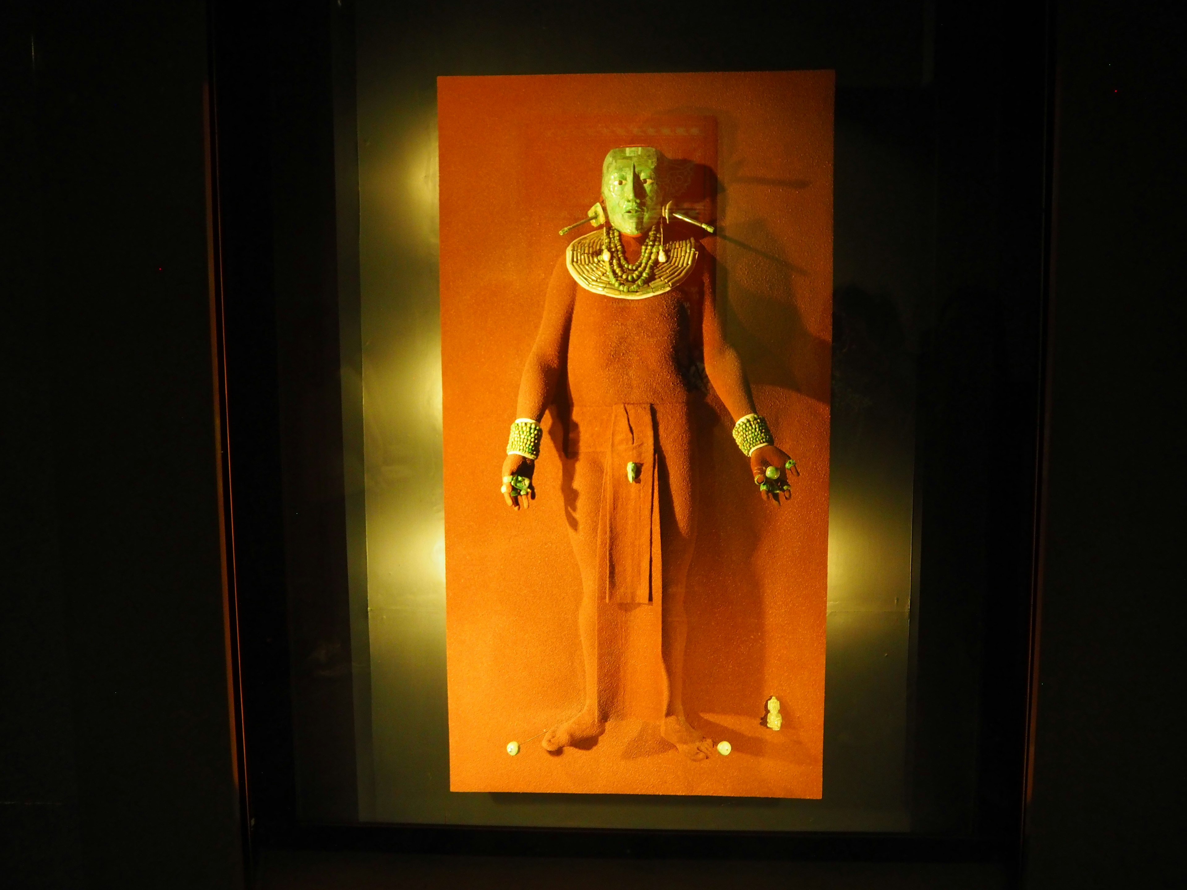 A decorated figure statue with a green face and metallic ornaments standing against a red background