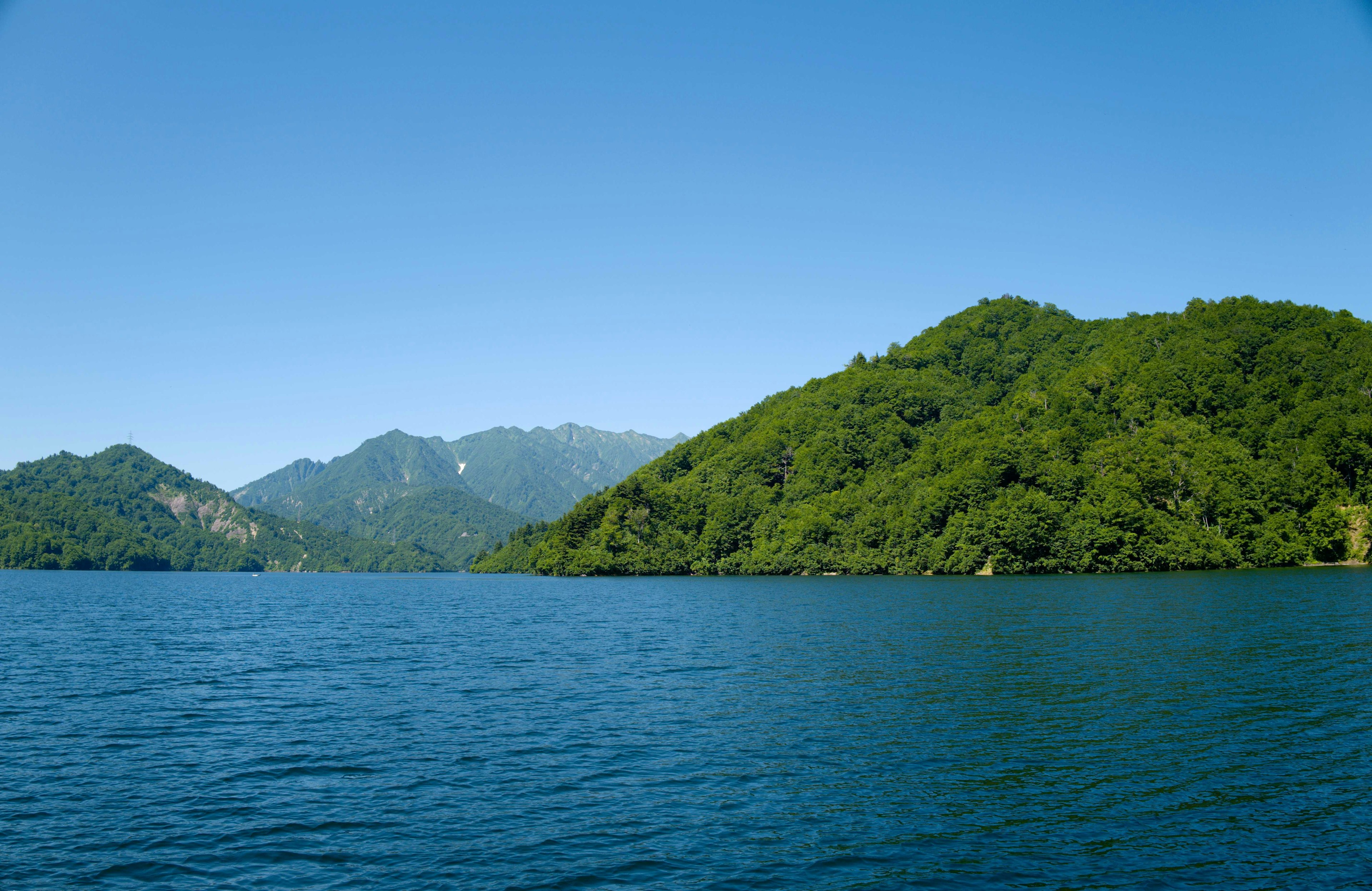 Pemandangan danau tenang dengan langit biru cerah dan pegunungan hijau