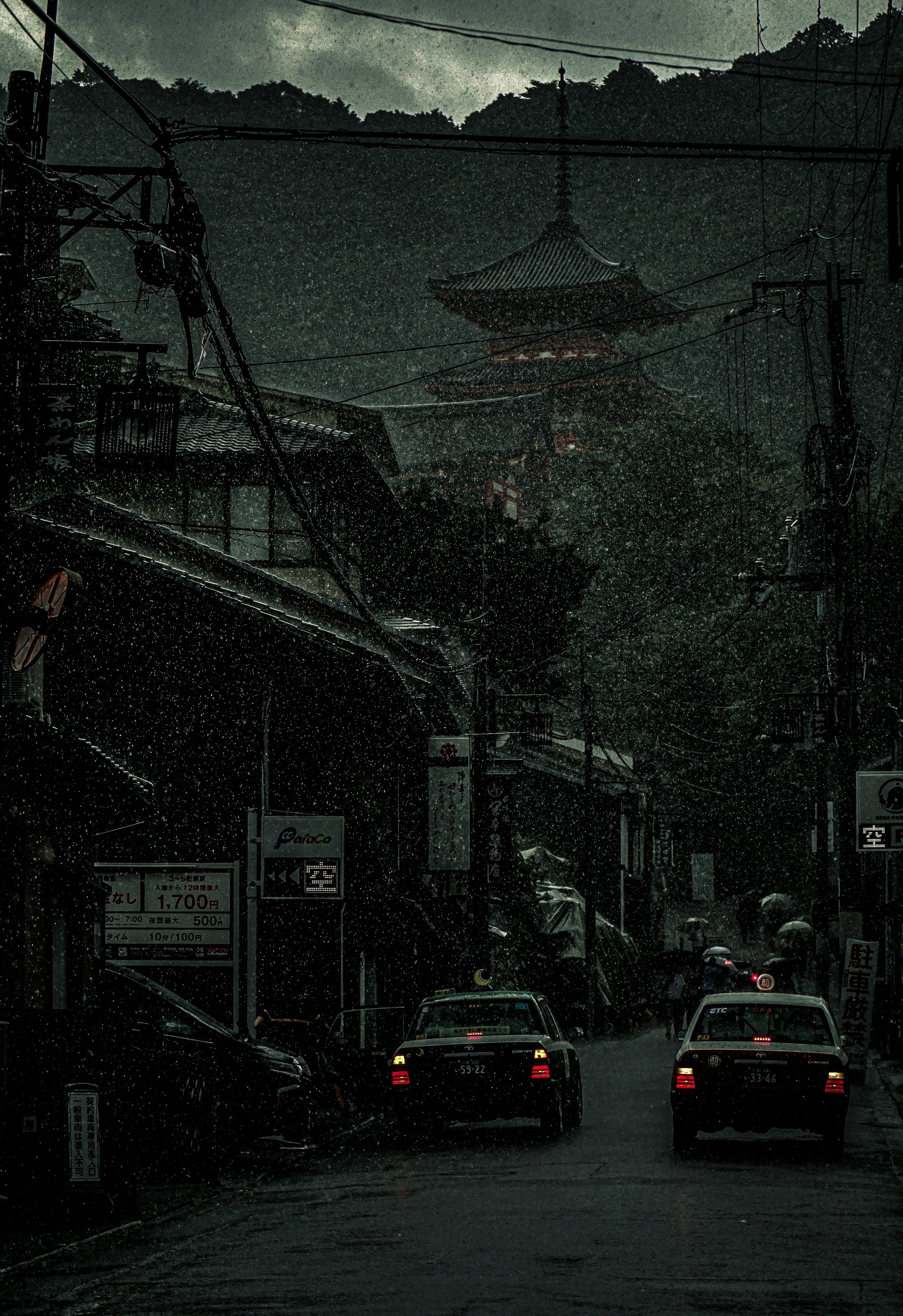 暗い街の通りに沿った車と山の上に見える寺