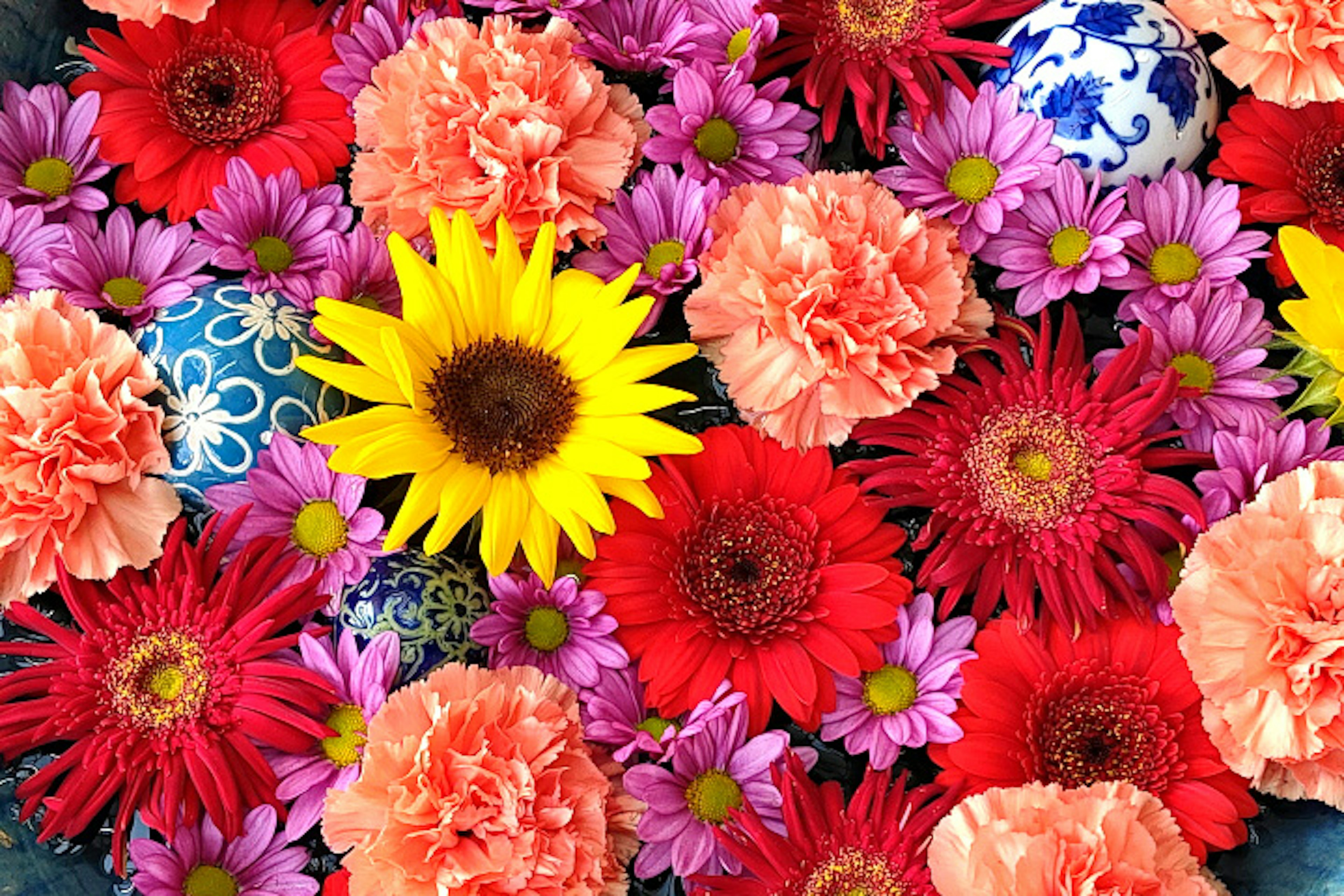 Colorful arrangement of flowers featuring a yellow sunflower and blue patterned eggs