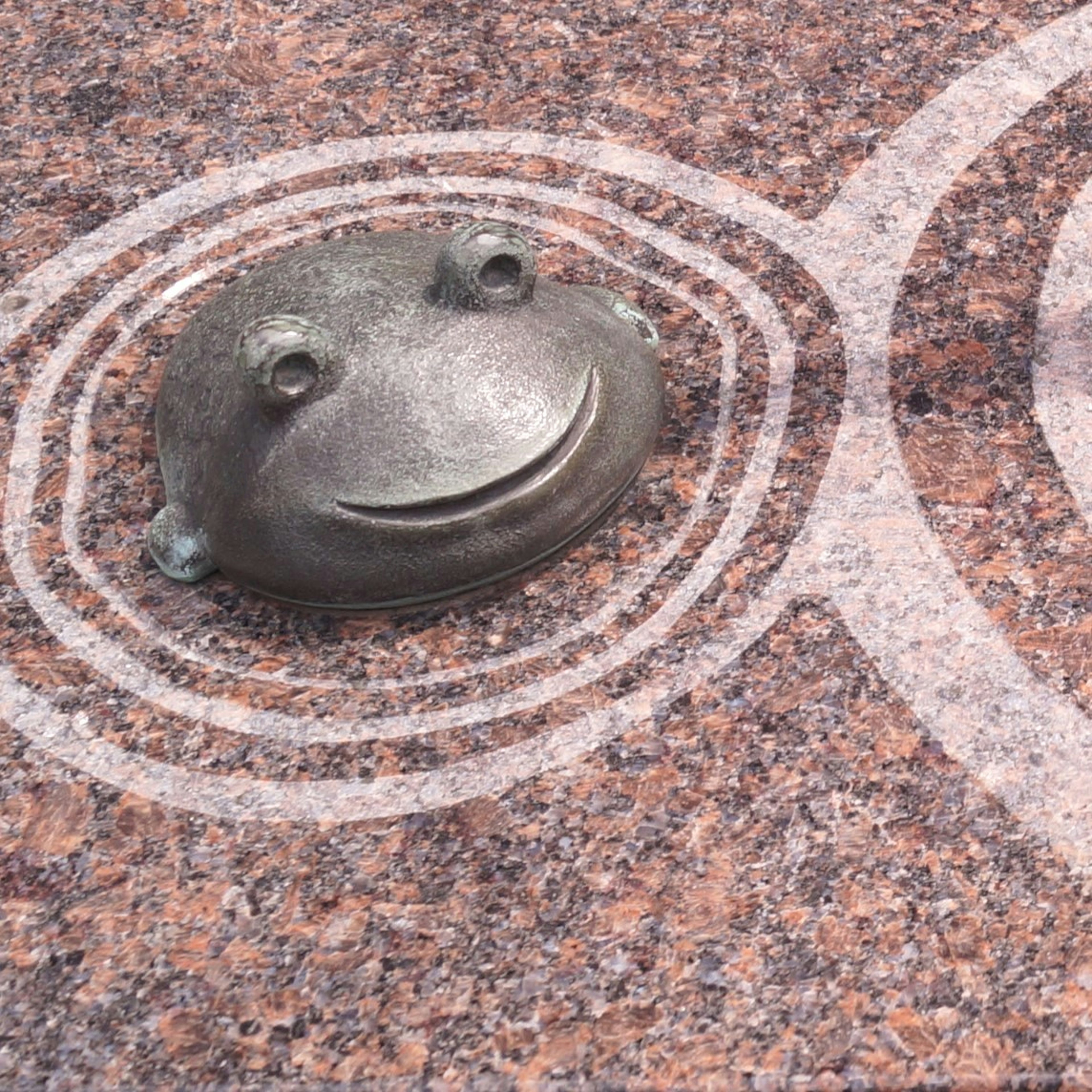 A smiling frog sculpture on textured stone surface with ripple design